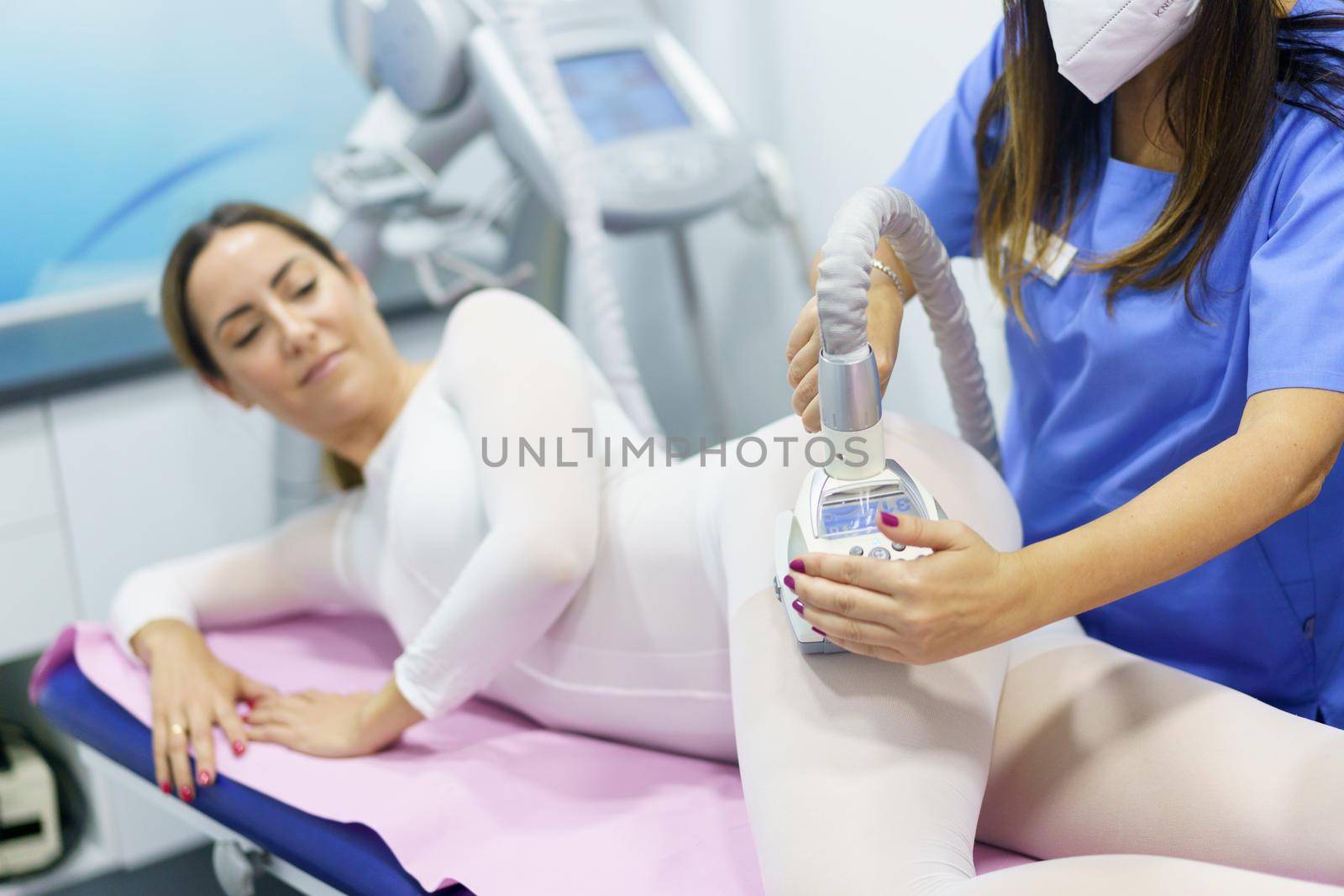 Middle-aged woman in special white suit having a anti cellulite massage with spa apparatus