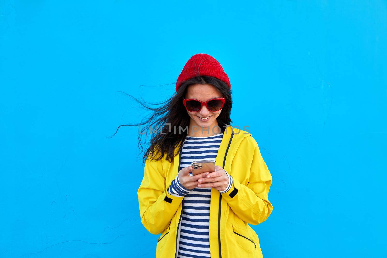 Woman in colorful outfit using smartphone blue background by Demkat