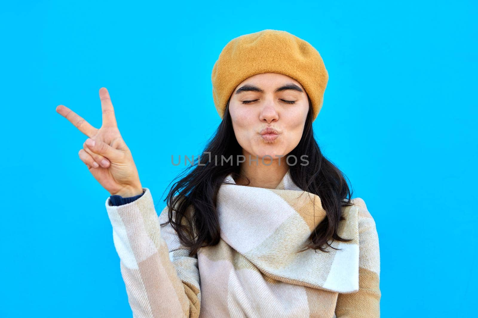 Photo of lovely dreamy lady blow air kiss show v-sign close eyes wear beige beret and coat isolated biue color background