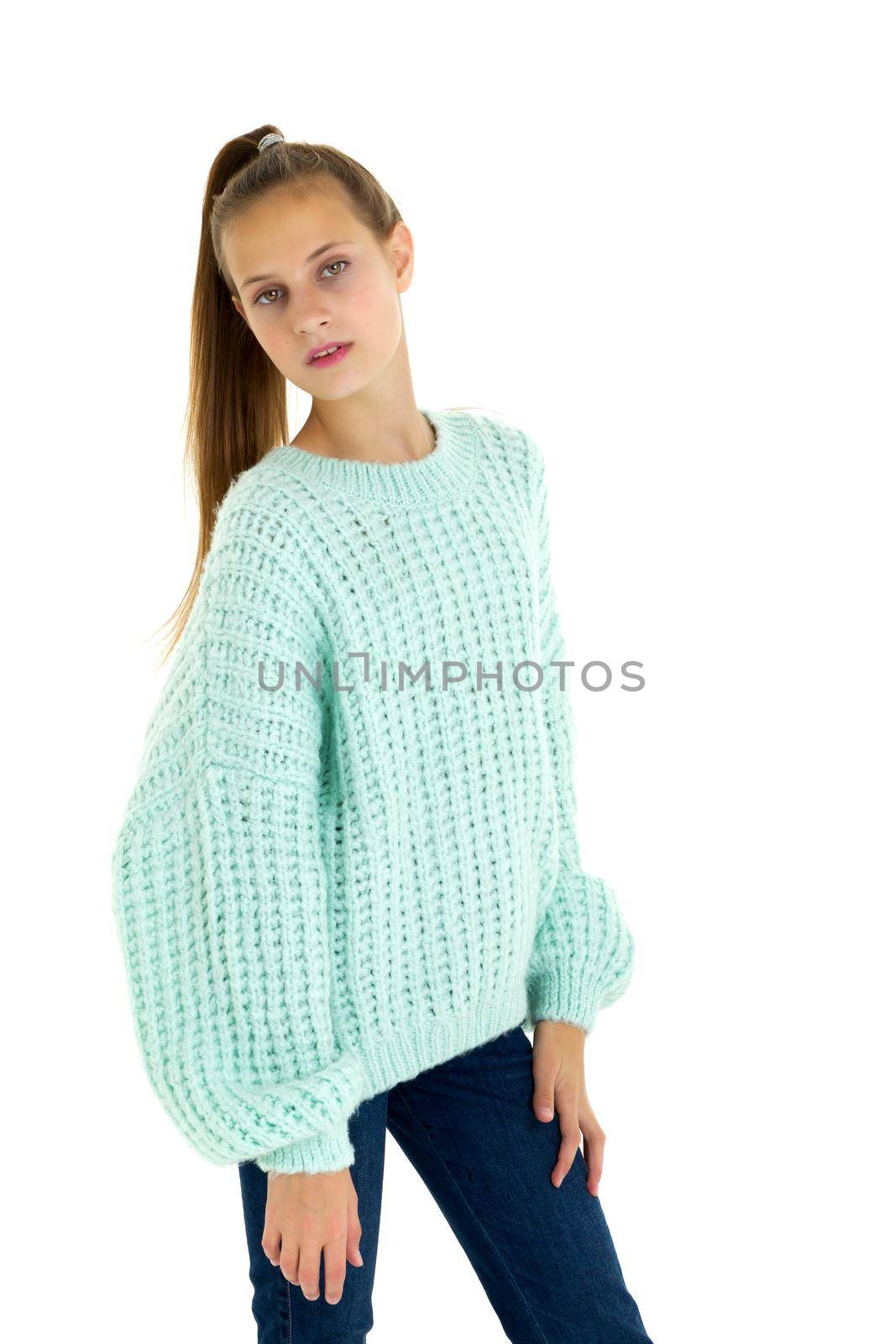 Pretty stylish teenage girl in fashionable outfit. Teenage girl with ponytail wearing warm oversized light blue sweater and jeans posing half turned to the camera on isolated white background