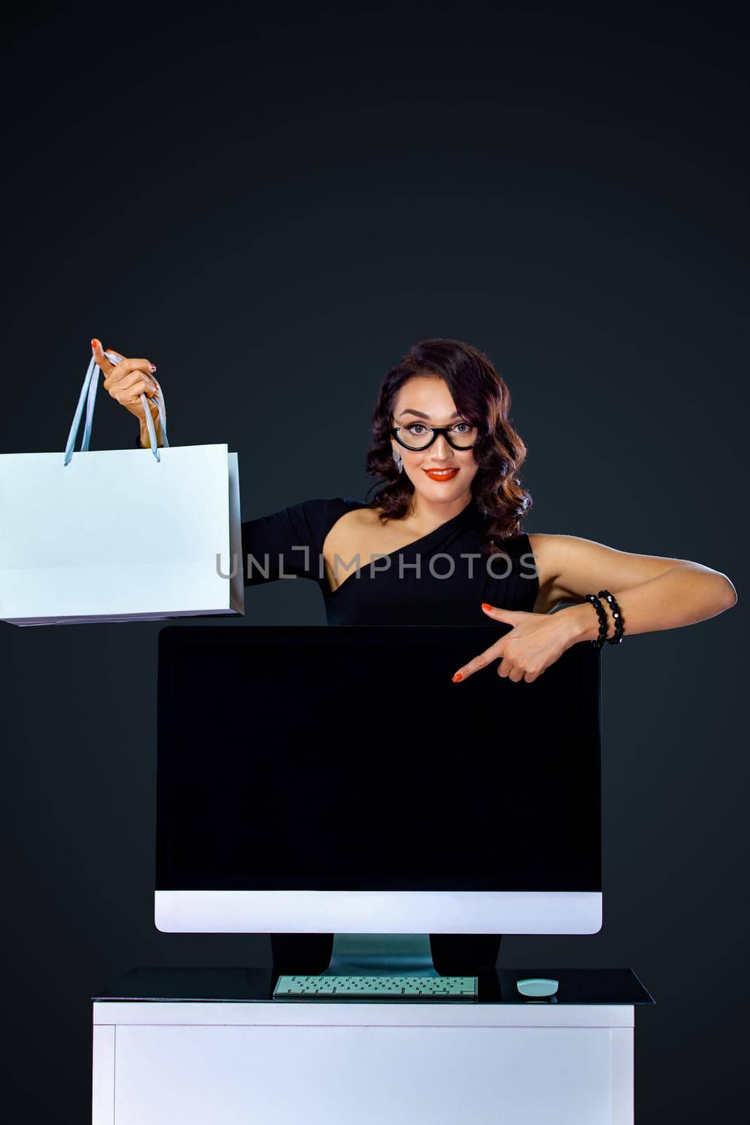 Black friday and Cyber Monday sale concept for shop. Shopping woman holding white bag and pointing on monitor isolated on dark background by MikeOrlov