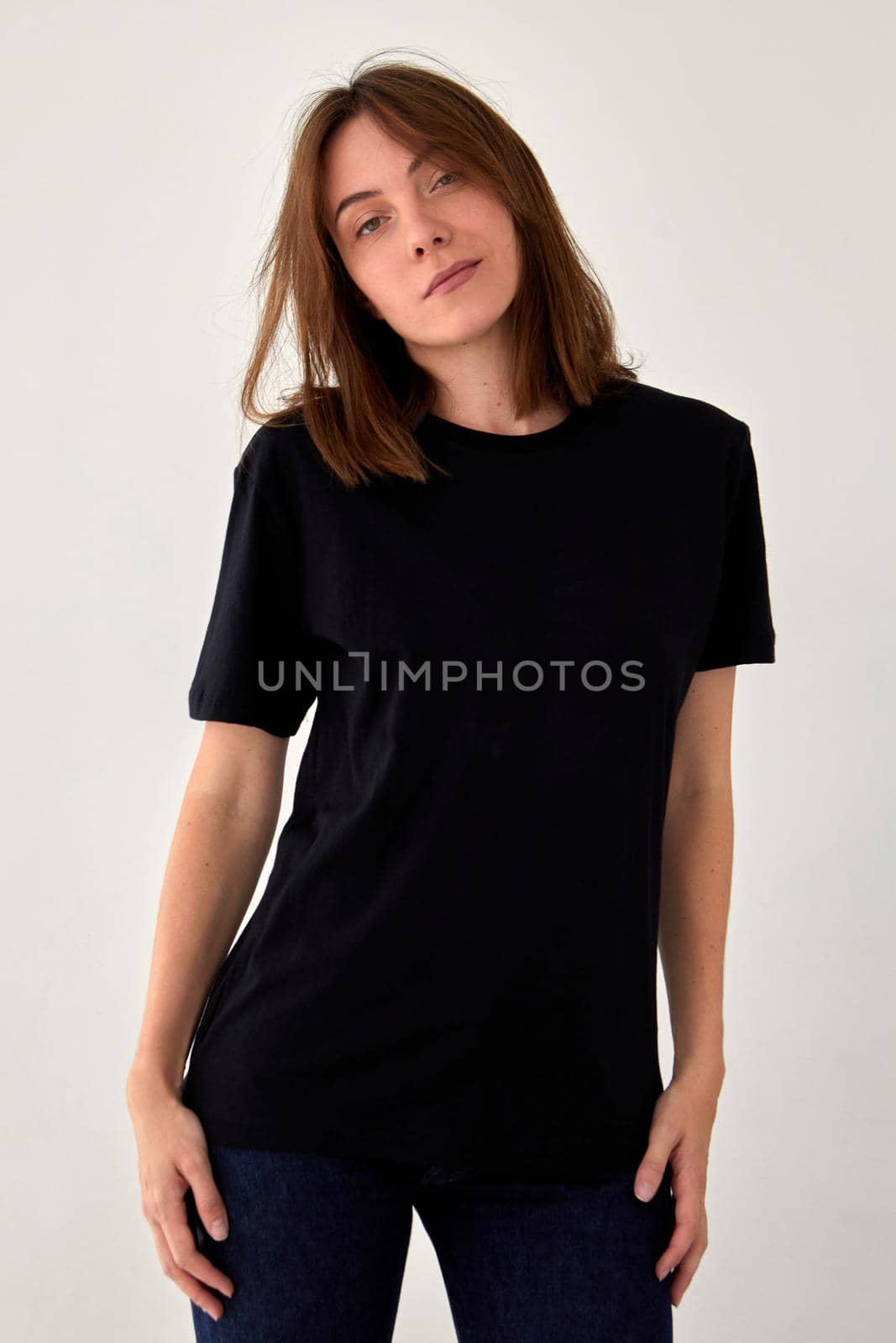 Serene young female wearing casual black t shirt looking at camera on white background in studio
