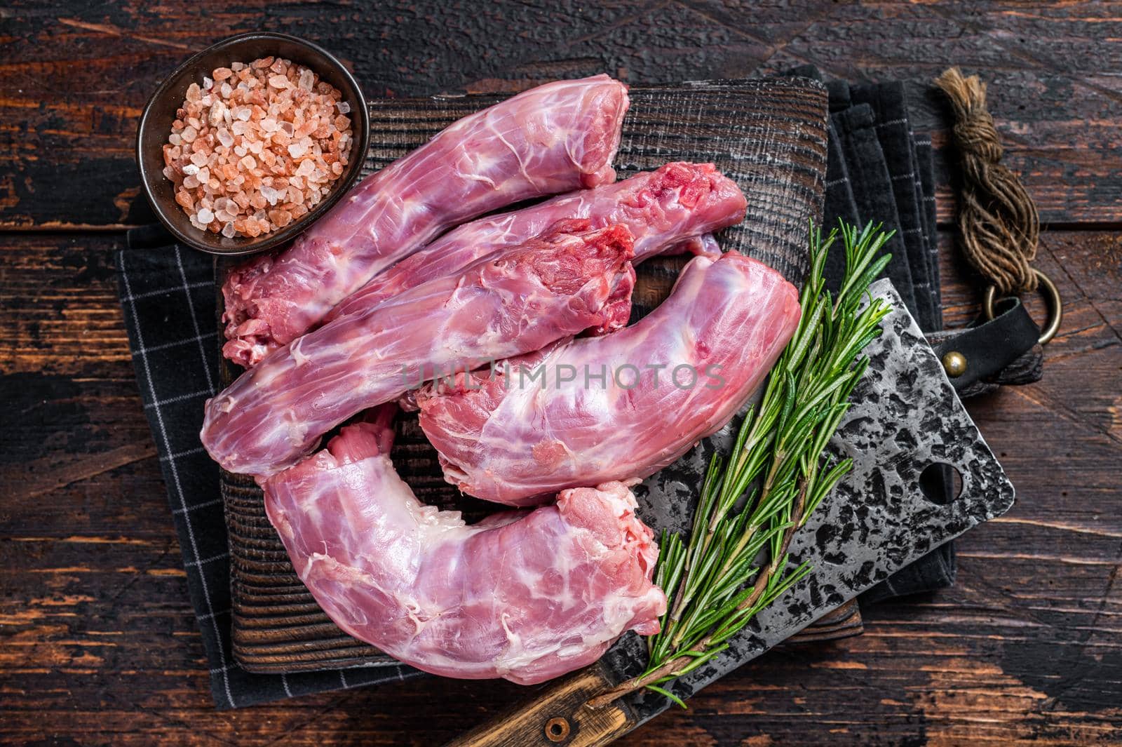 Uncooked Raw Turkey necks meat on a butcher wooden board with cleaver. Dark wooden background. Top View.