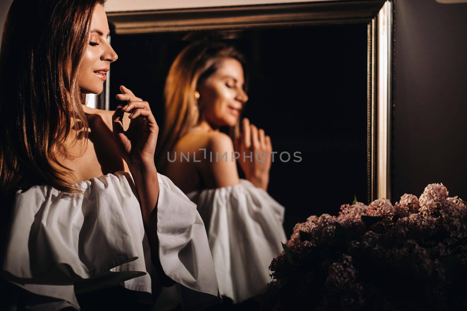 Beautiful girl in the mirror reflection at home. Girl before the holiday near the home mirror.A girl in a white dress with long hair is going to a party at home.