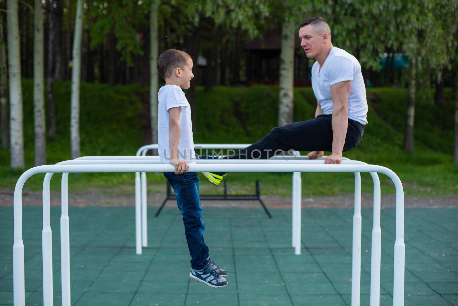 Caucasian man trains a boy on the uneven bars on the playground. Dad and son go in for outdoor sports. by mrwed54