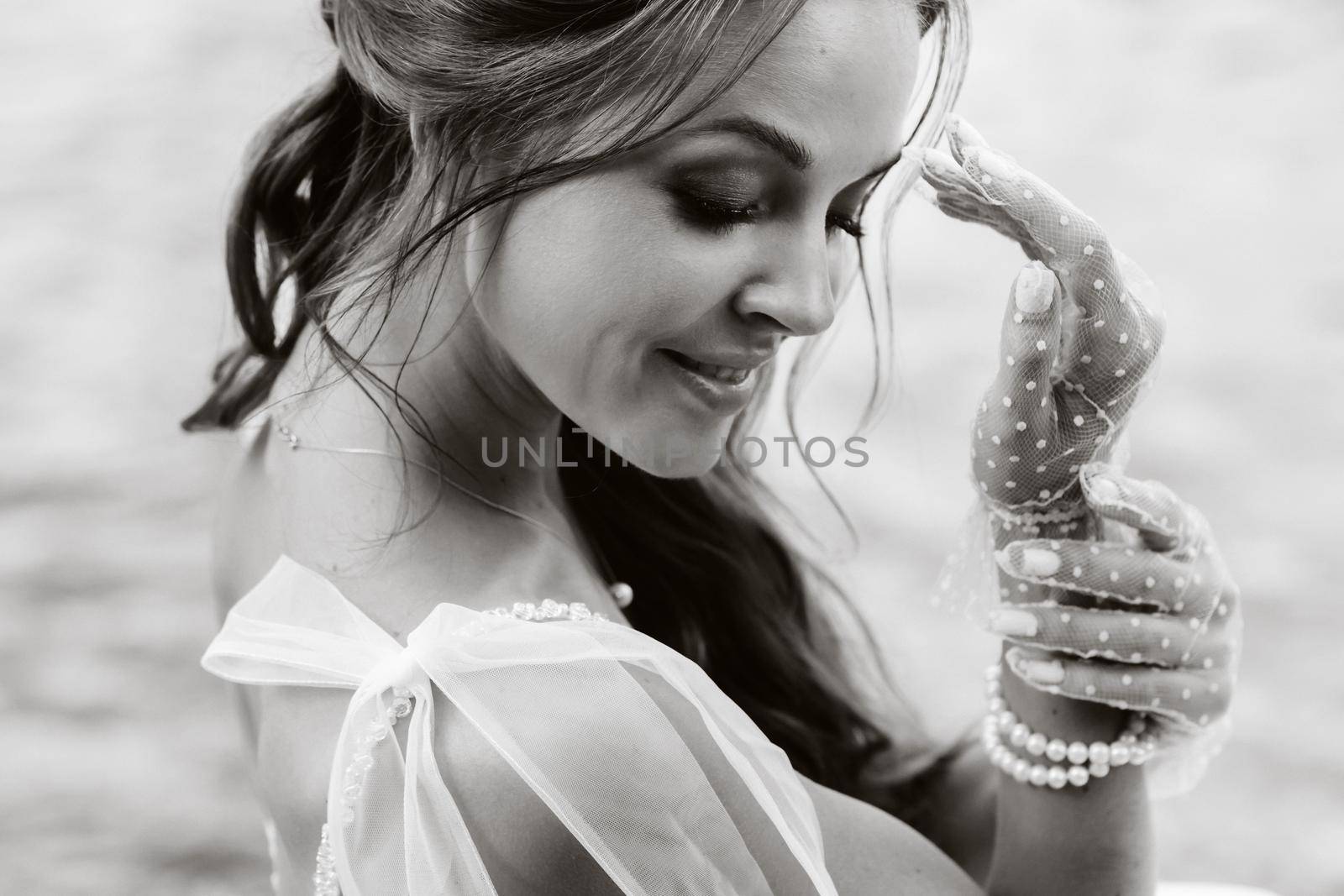 An elegant bride in a white dress, gloves and bare feet is sitting near a waterfall in the Park enjoying nature.A model in a wedding dress and gloves at a nature Park.Belarus. black and white photo by Lobachad