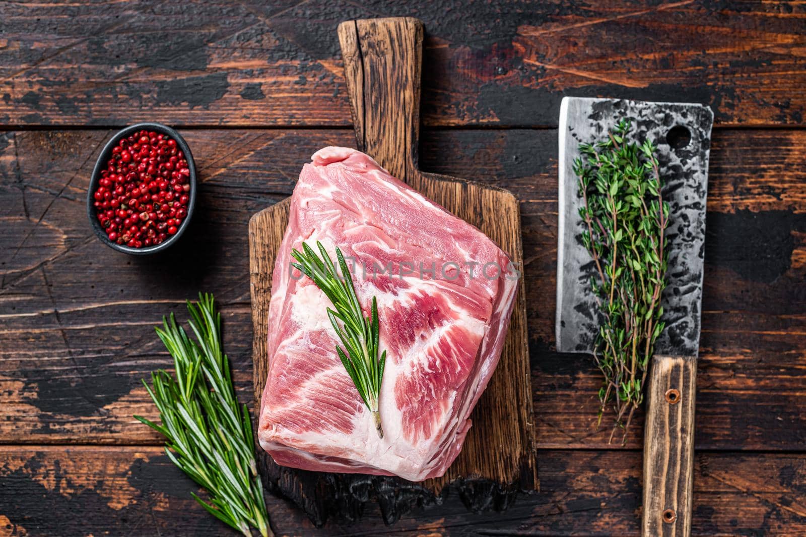 Pork Shoulder raw meat for fresh steaks on wooden cutting board with butcher cleaver. Dark wooden background. Top view.