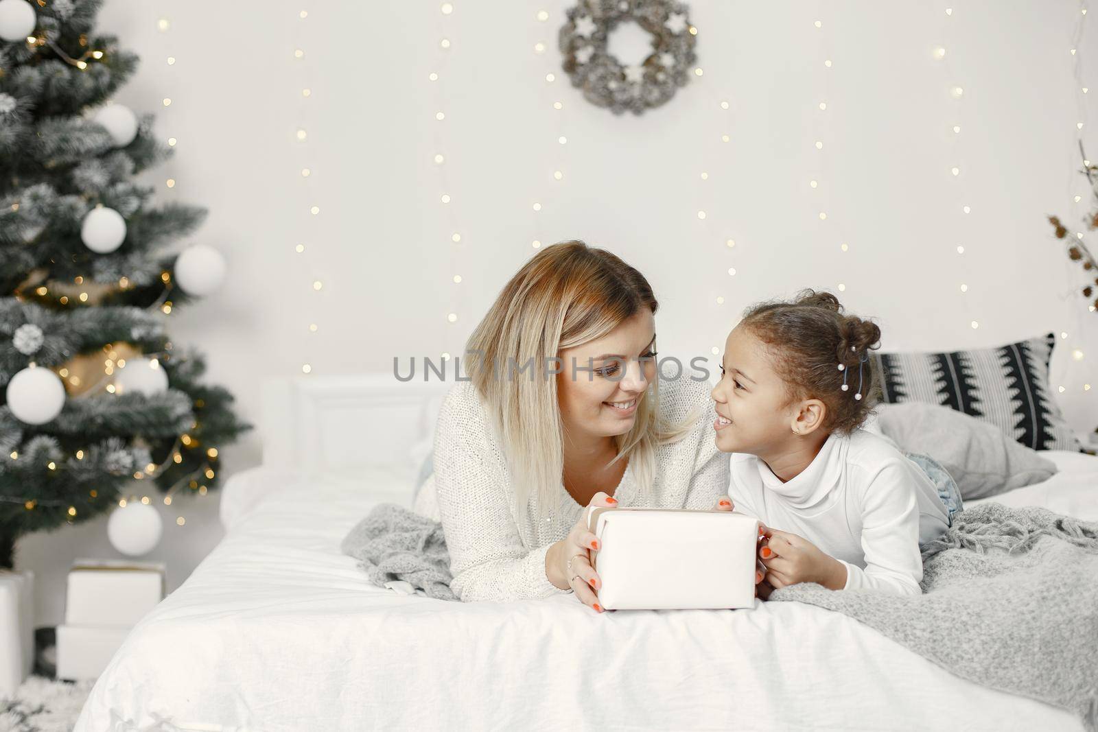 People reparing for Christmas. Mother playing with her daughter. Family is resting in a festive room. Child in a sweater sweater.