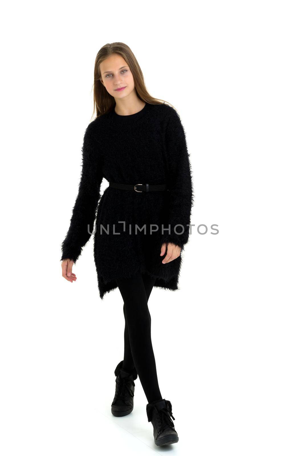Happy teenage girl in fashionable black outfit. Full length portrait of beautiful girl with long straight hair wearing black dress, stockings and boots standing against white background in studio