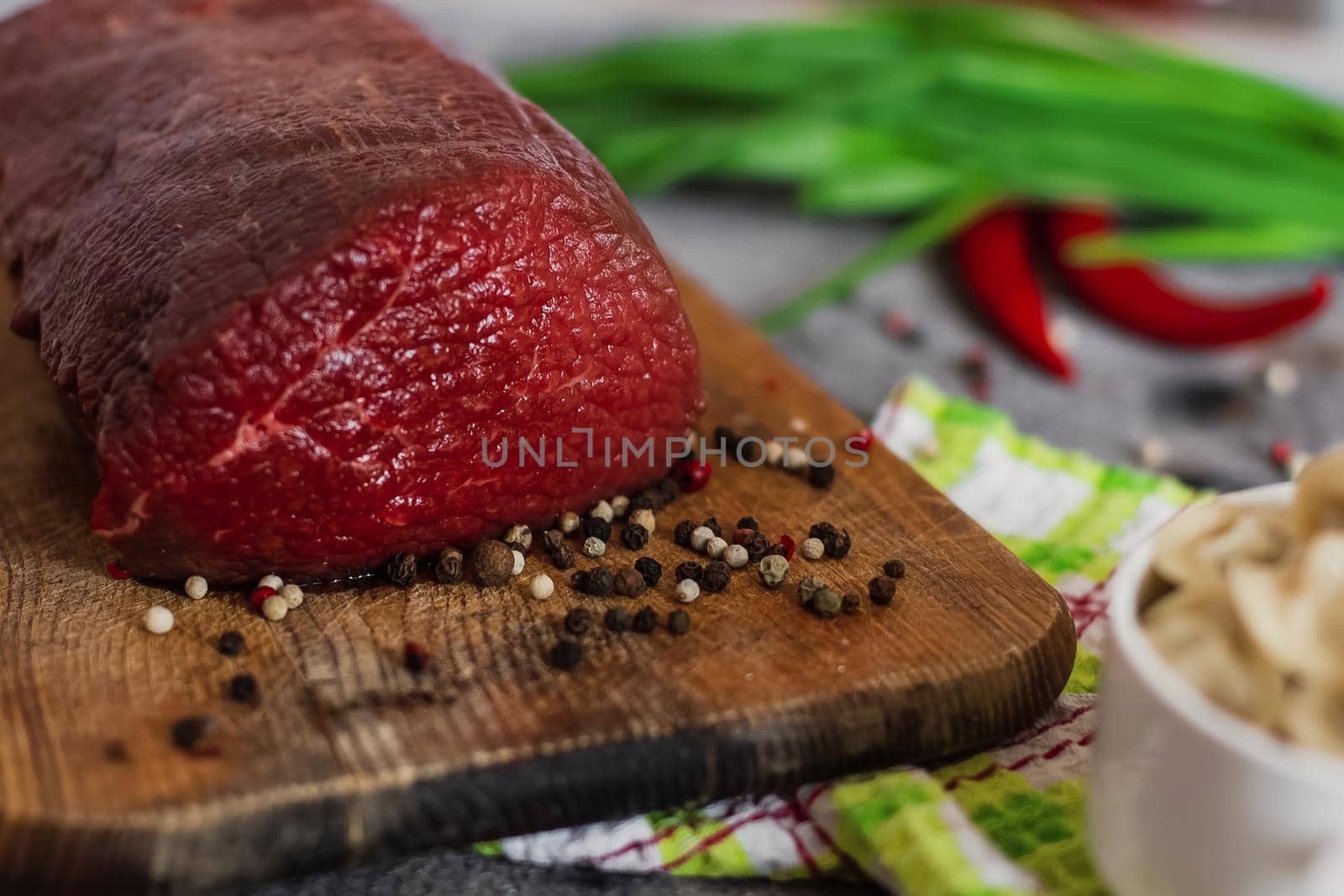 Raw meat. A large piece of beef chop on a wooden cutting board with pepper and spices.