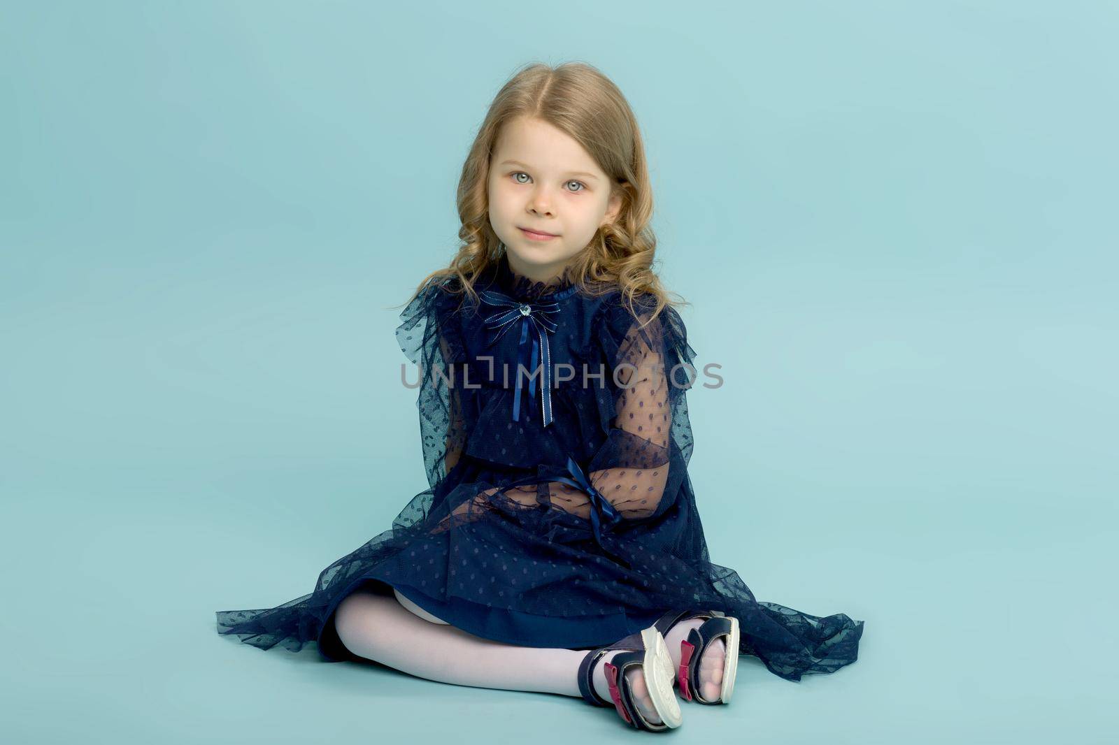 Happy little girl in blue dress sitting on floor by kolesnikov_studio
