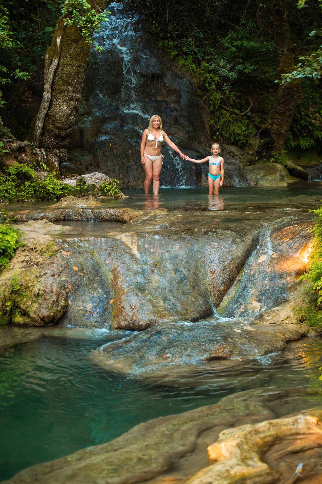Mom and daughter on a mountain river under a waterfall in the jungle.Turkey.