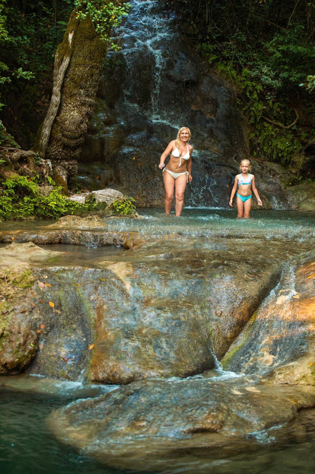 Mom and daughter on a mountain river under a waterfall in the jungle.Turkey. by Lobachad