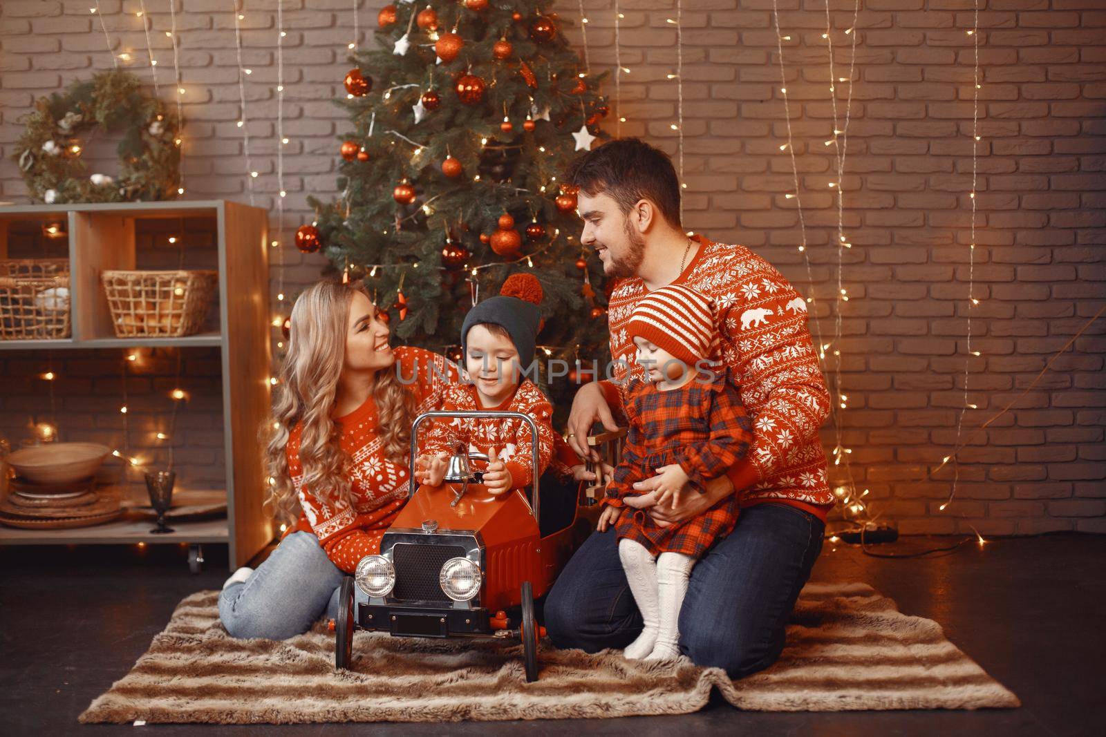 People reparing for Christmas. People playing with their daughter. Family is resting in a festive room. Child in a red dress.