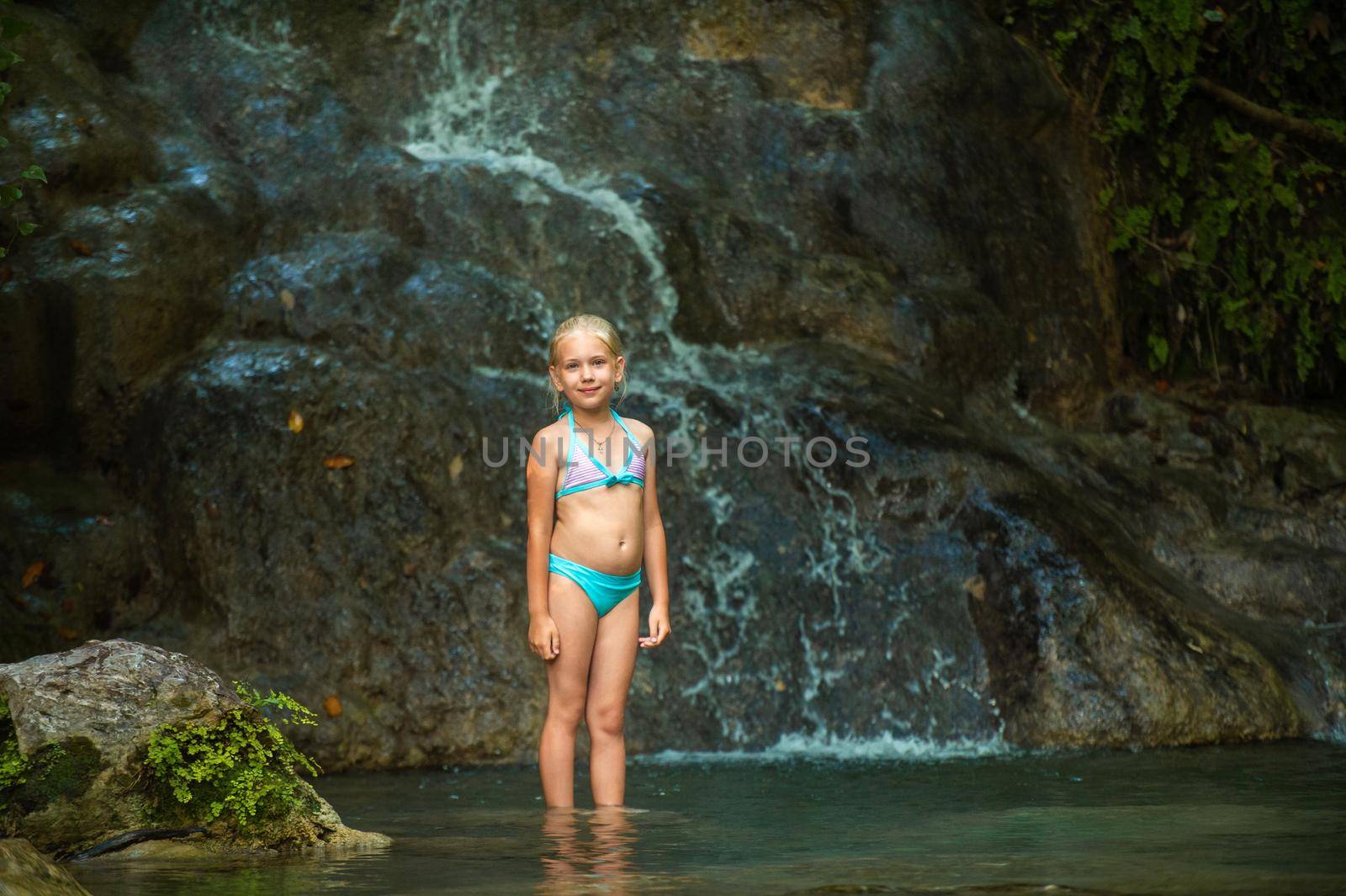 a little girl in a swimsuit at a waterfall in the jungle. Nature trip near a beautiful waterfall, Turkey.