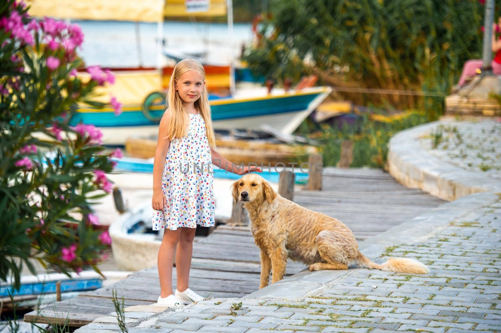 A little girl with a dog on the embankment by the river in a white sundress in the city of Dalyan. Turkey by Lobachad