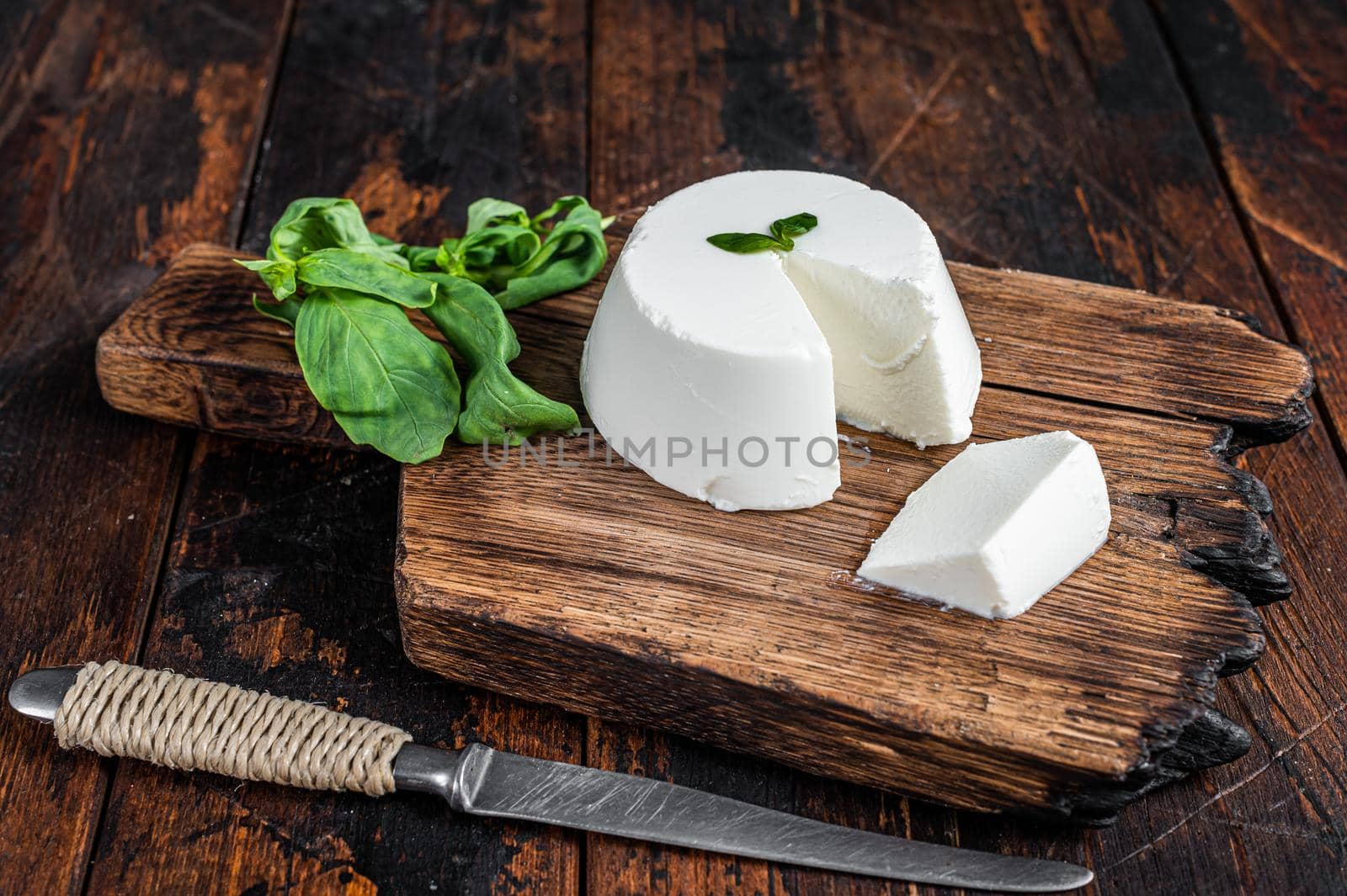 Fresh Ricotta cream Cheese on wooden board with basil. Dark wooden background. Top view.