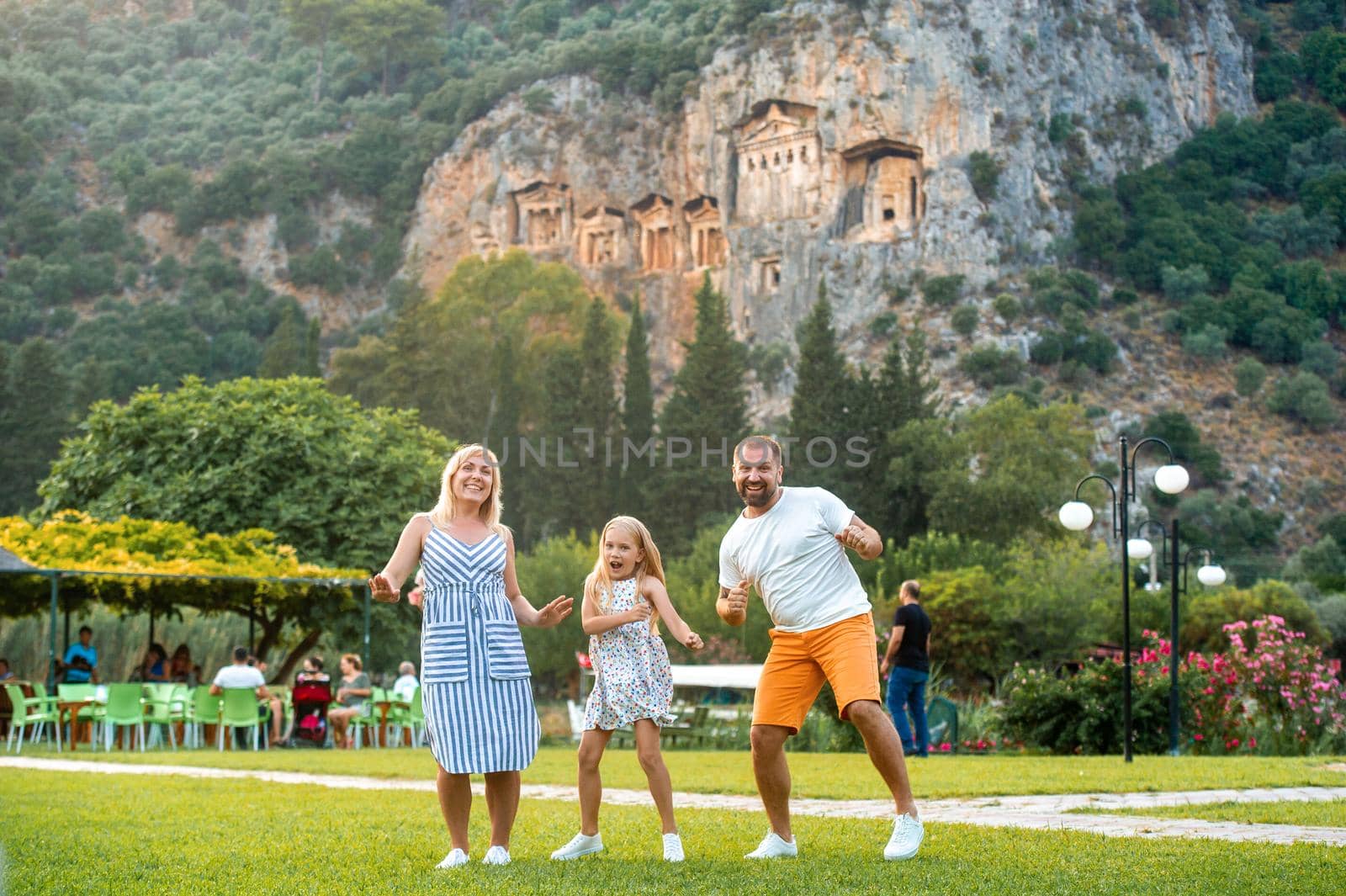 A happy family stands on the background of a mountain in the city of Dalyan.People near Lycian tombs in Turkey by Lobachad