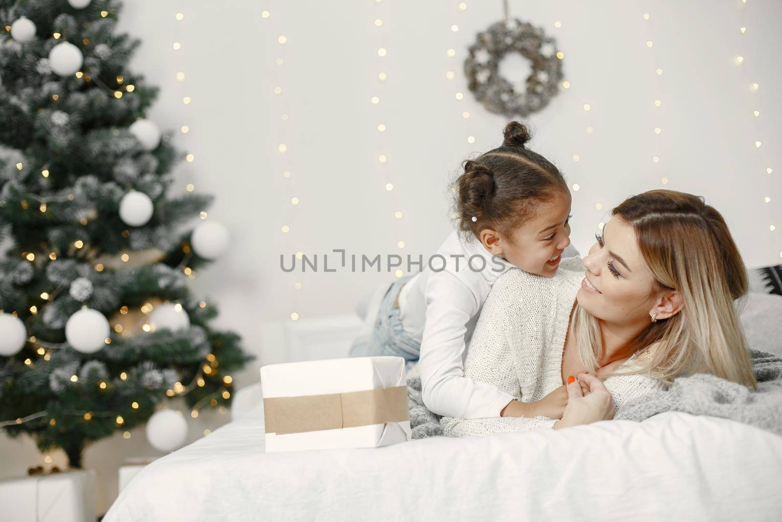 People reparing for Christmas. Mother playing with her daughter. Family is resting in a festive room. Child in a sweater sweater.