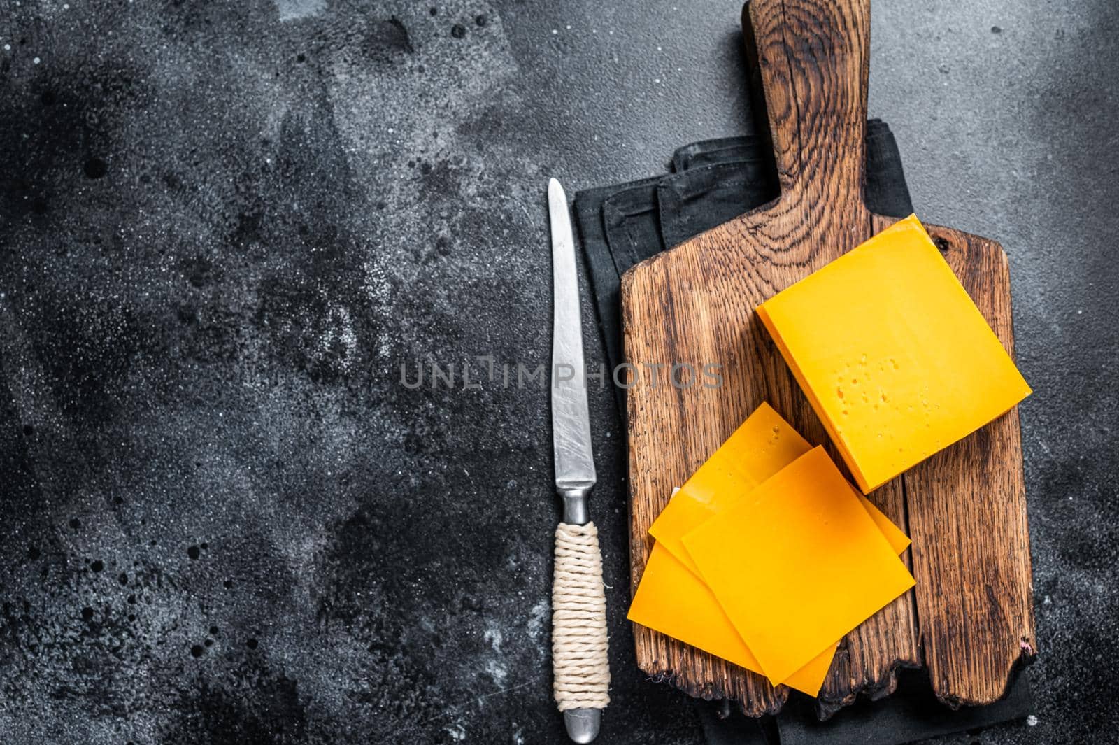 Slices of Cheddar Cheese on a wooden cutting board. black background. Top view. Copy space.