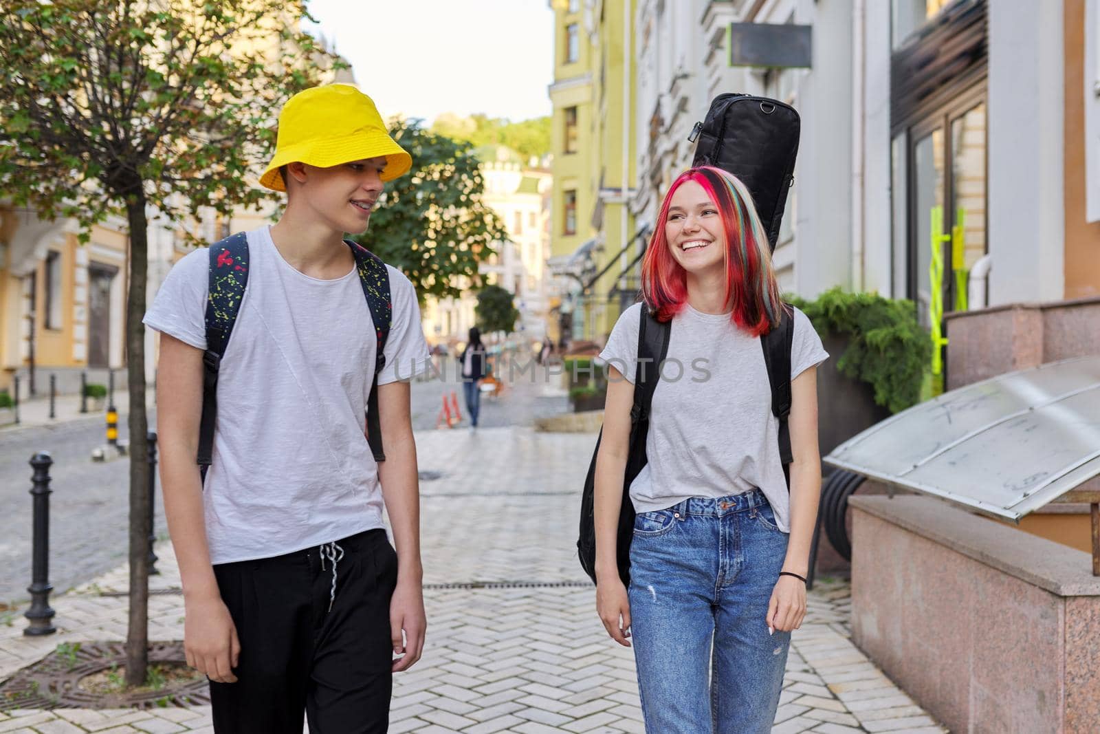 Creative teenagers guy and girl walking and talking along city street by VH-studio