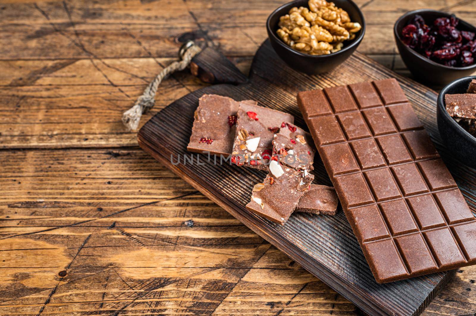 Dark chocolate bar with hazelnuts, peanuts, cranberries and freeze dried raspberries on a wooden board. wooden background. Top view. Copy space.