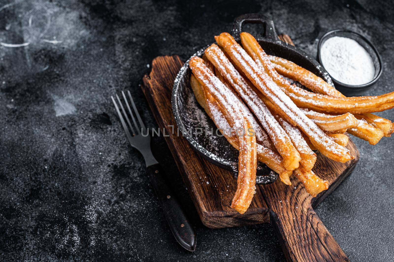 Traditional Mexican dessert churros with sugar powder in a pan. Black background. Top view. Copy space.