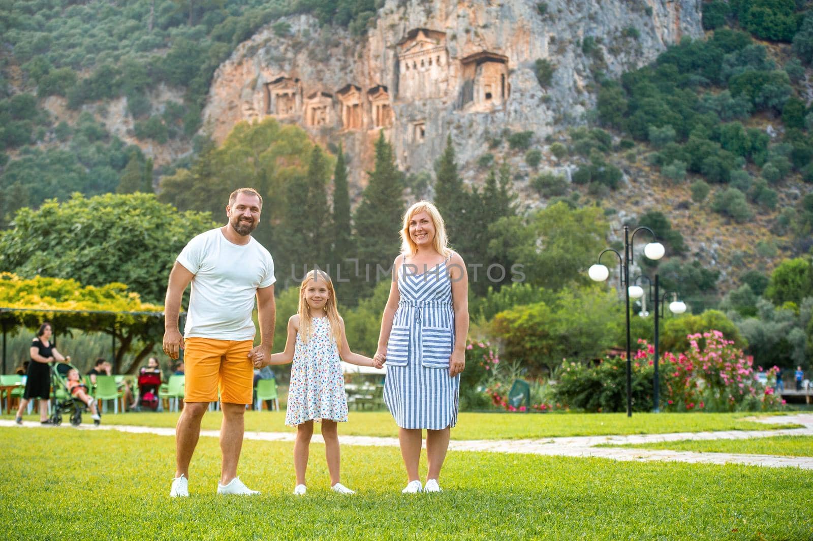 A beautiful family stands on the background of a mountain in the city of Dalyan.People near Lycian tombs in Turkey by Lobachad