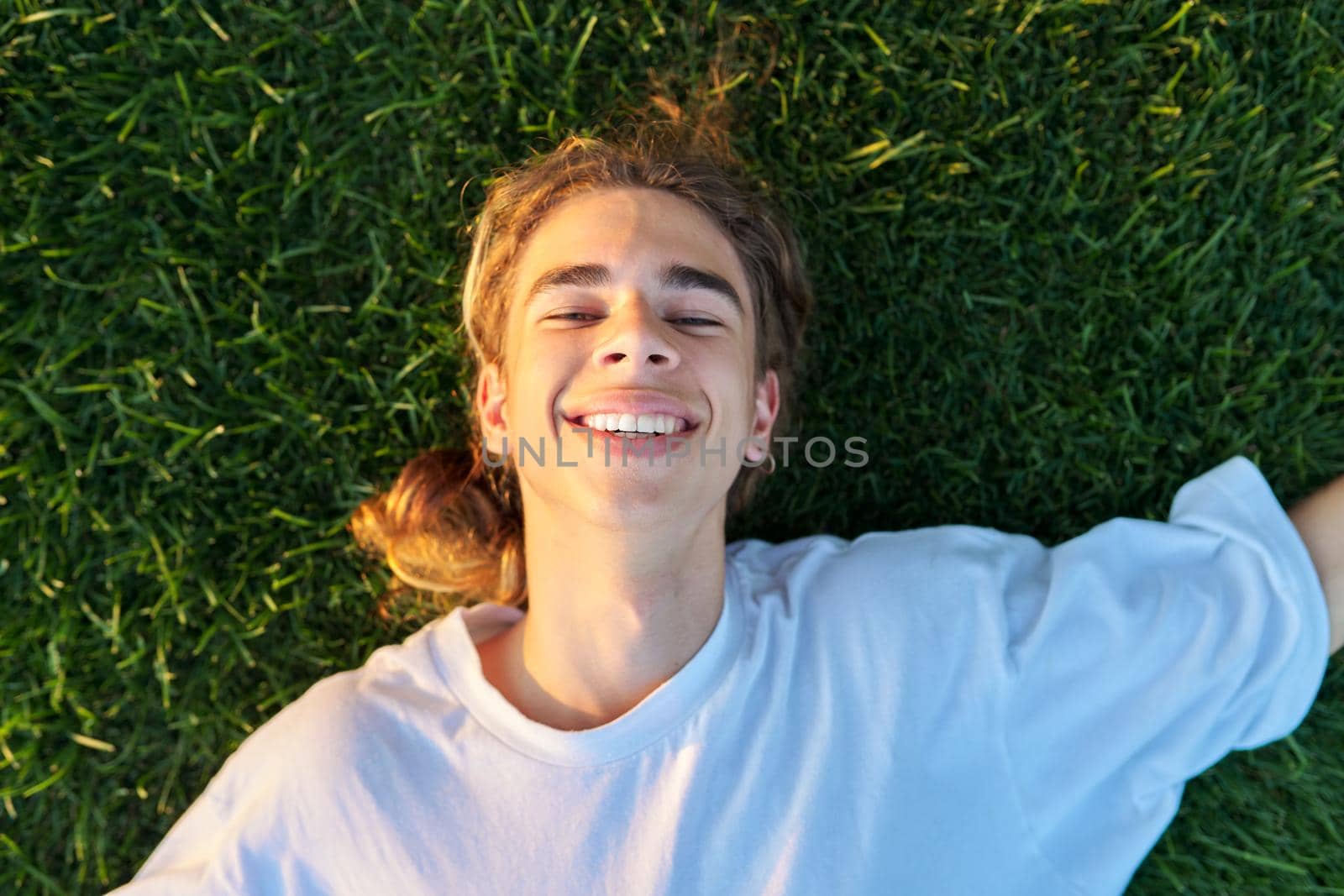 Close-up face of handsome guy 16, 17 years old on green grass, top view by VH-studio