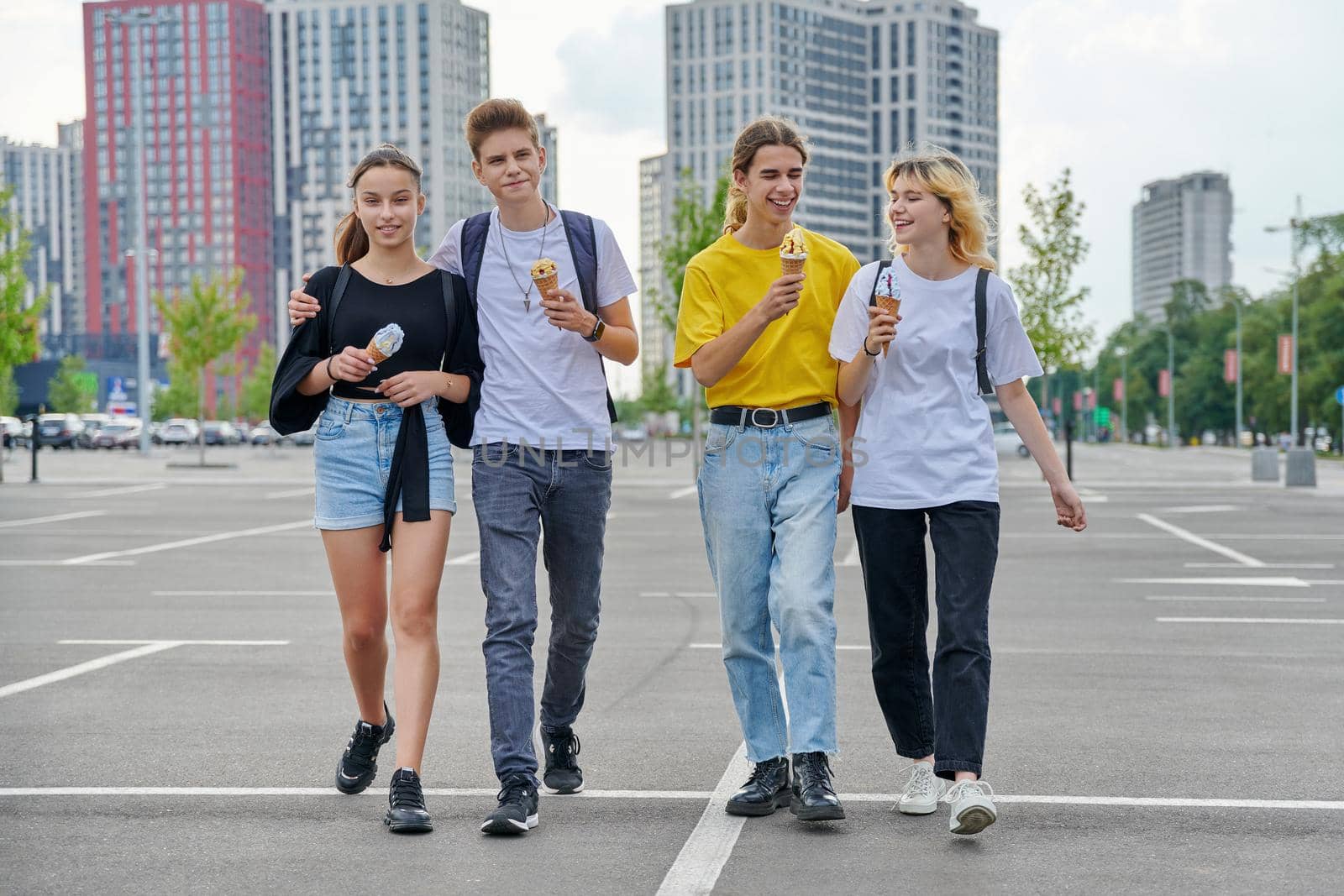 Group portrait of happy teenagers walking together with ice cream. Four smiling young people in city, lifestyle, friendship, adolescence, urban style, summer, leisure, youth concept