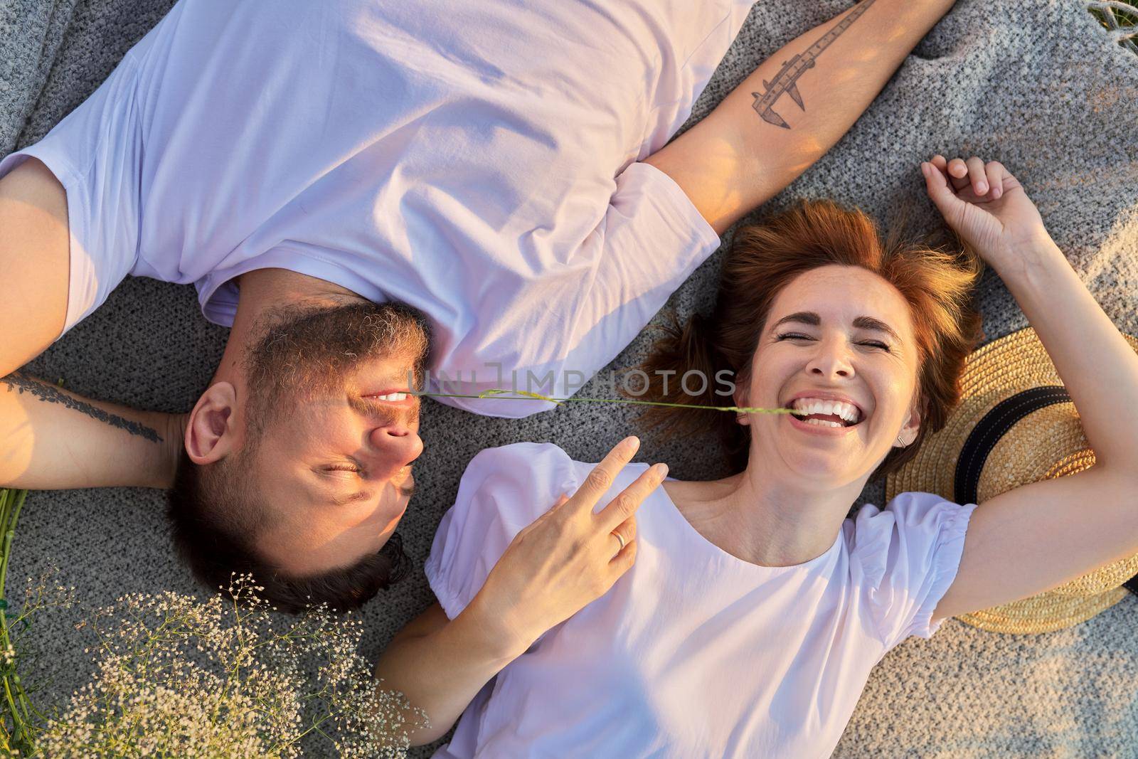 Happy romantic middle aged couple, top view on smiling faces lying on blanket, in sunny sunset light. Love, relationships, dating, family, lifestyle, people 30s 40s age concept