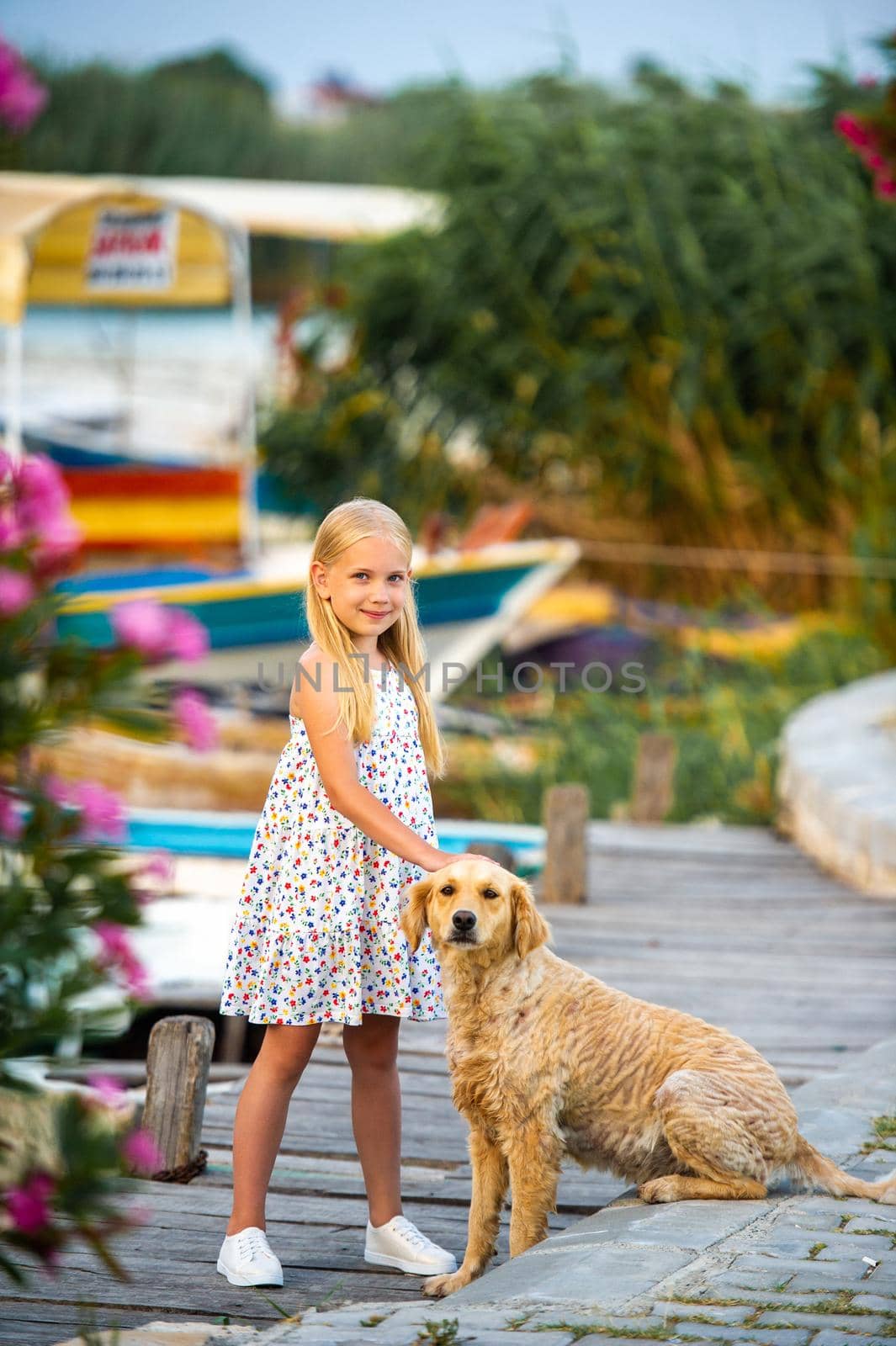 A little girl with a dog on the embankment by the river in a white sundress in the city of Dalyan. Turkey.
