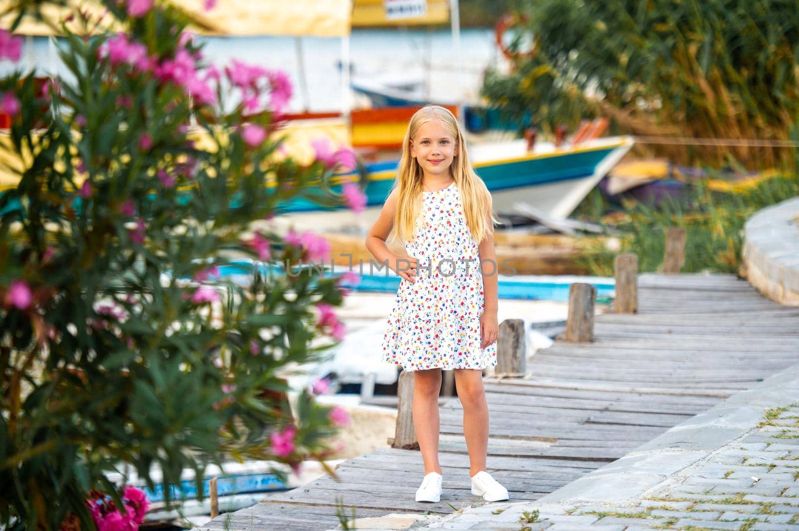 A little girl on the embankment by the river in a white sundress in the city of Dalyan. Turkey by Lobachad