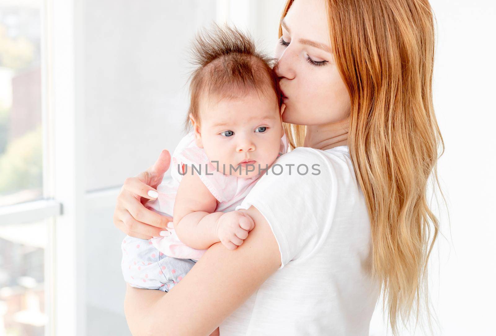 Happy mother kissing cute baby indoors