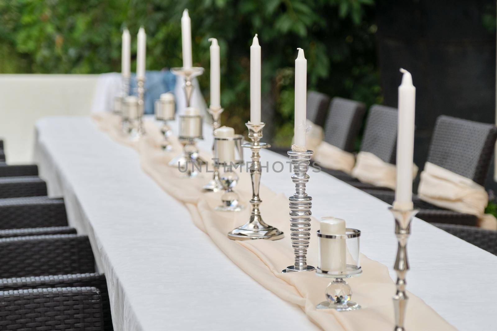 Decoration of events, close-ups of decor details, beginning of table setting. Table with white tablecloth and candlesticks in the outdoor garden