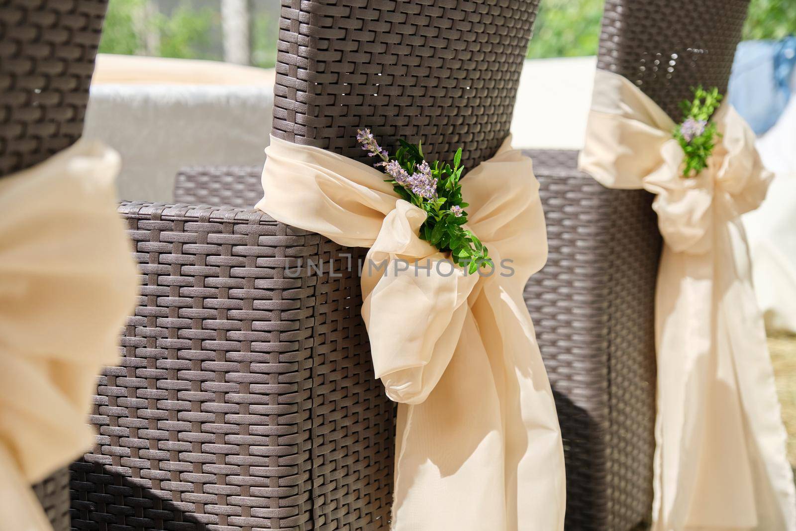 Close-up of rattan garden chairs decorated with textiles with flowers for a party, ceremony by VH-studio