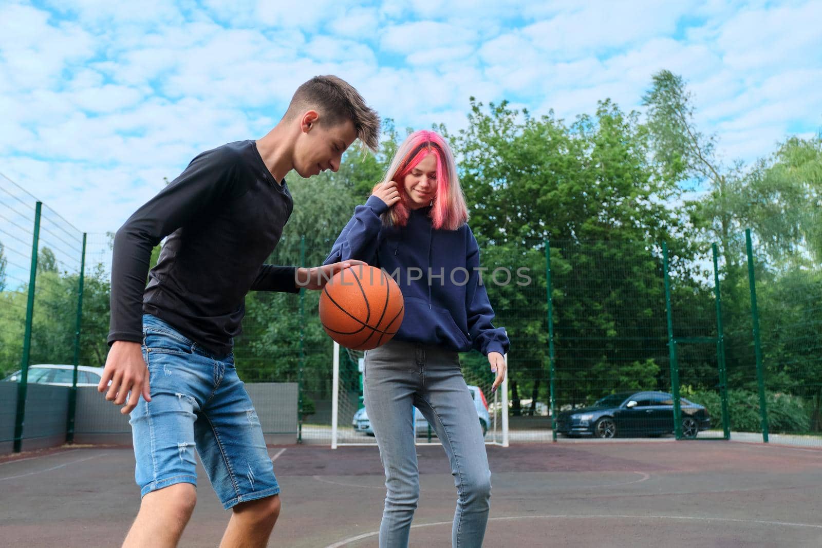 Active healthy lifestyle of youth, hobbies and leisure, teenagers guy and girl on an outdoor basketball court playing street basketball