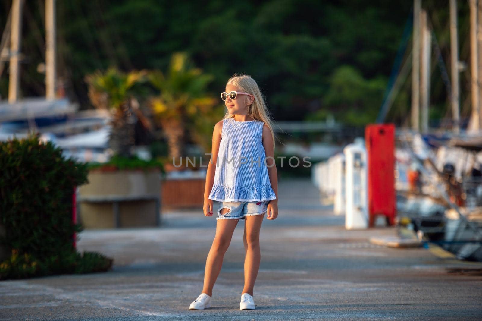 Portrait of a cute smiling little girl with glasses.A girl in shorts and a blue T-shirt at sunset by the sea.Turkey by Lobachad