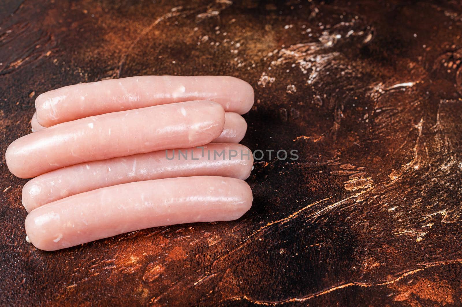 Raw chicken and turkey meat sausages on butcher table. Dark background. Top view. Copy space.