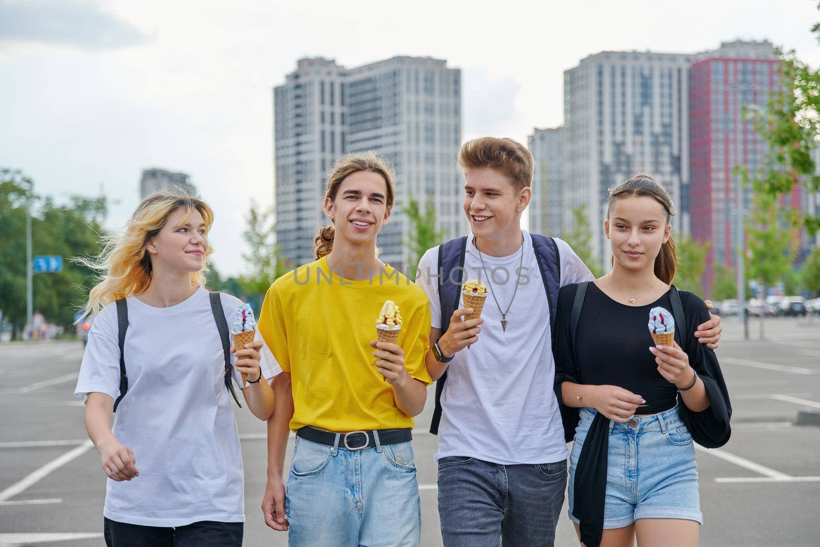 Group portrait of happy teenagers walking together with ice cream. Four smiling young people in city, lifestyle, friendship, adolescence, urban style, summer, leisure, youth concept