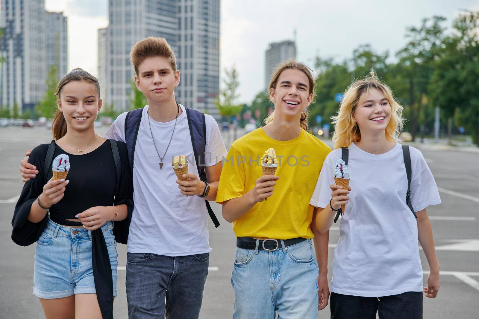 Group portrait of happy teenagers walking together with ice cream. Four smiling young people in city, lifestyle, friendship, adolescence, urban style, summer, leisure, youth concept