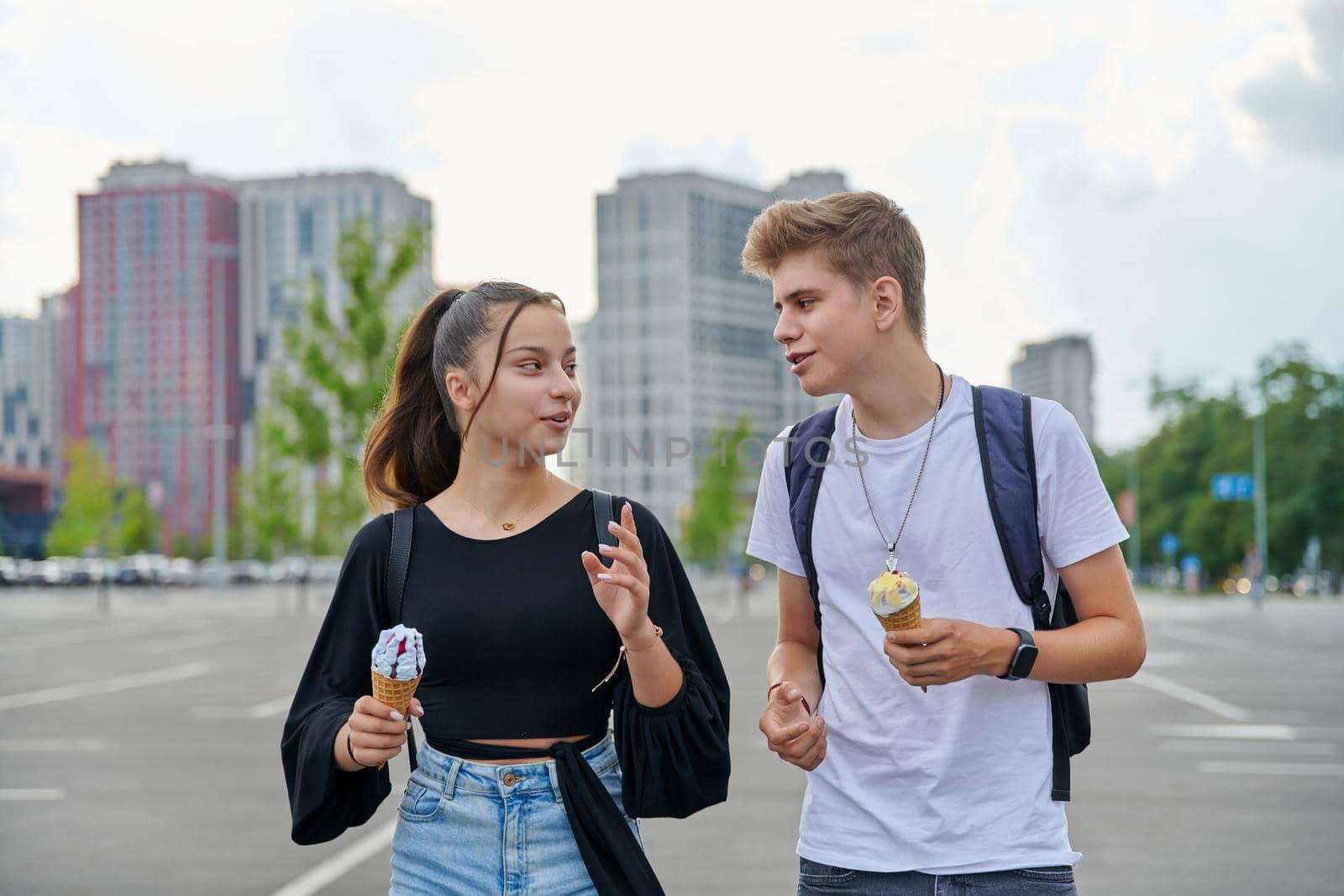 Happy talking couple of teenagers walking together in city, guy and teenage girl with ice cream, friendship, relationship, summer, leisure, lifestyle, adolescence concept