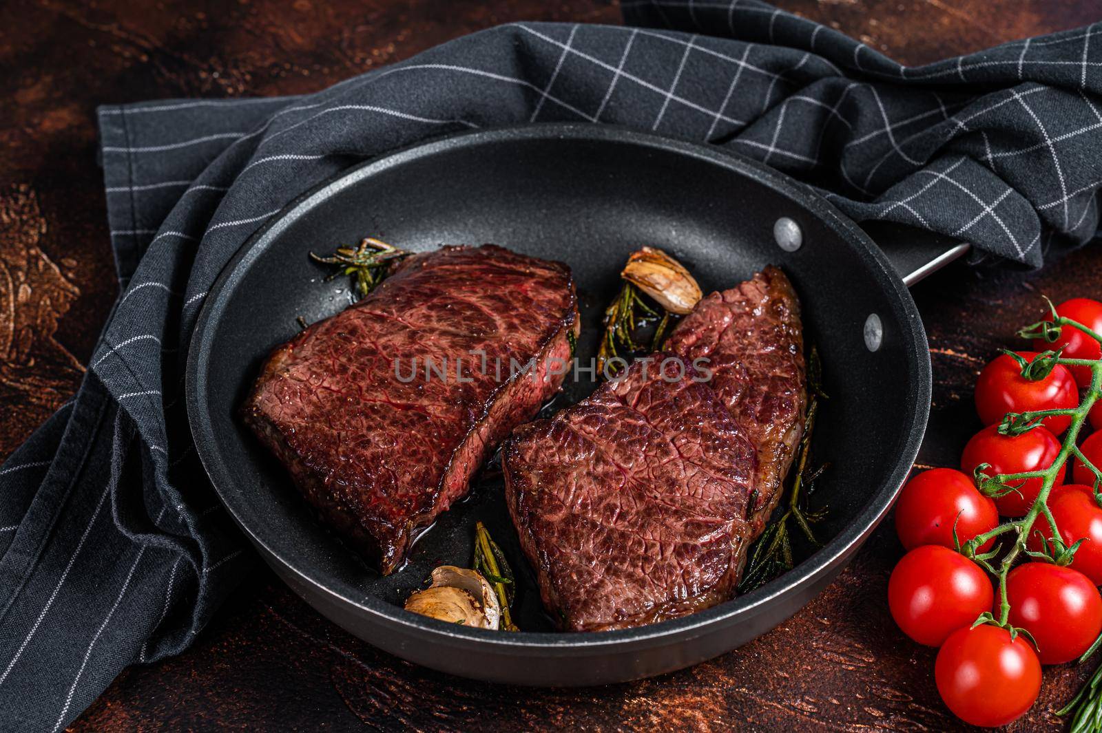 Grilled denver beef meat steak in a pan with rosemary. Dark background. Top view.