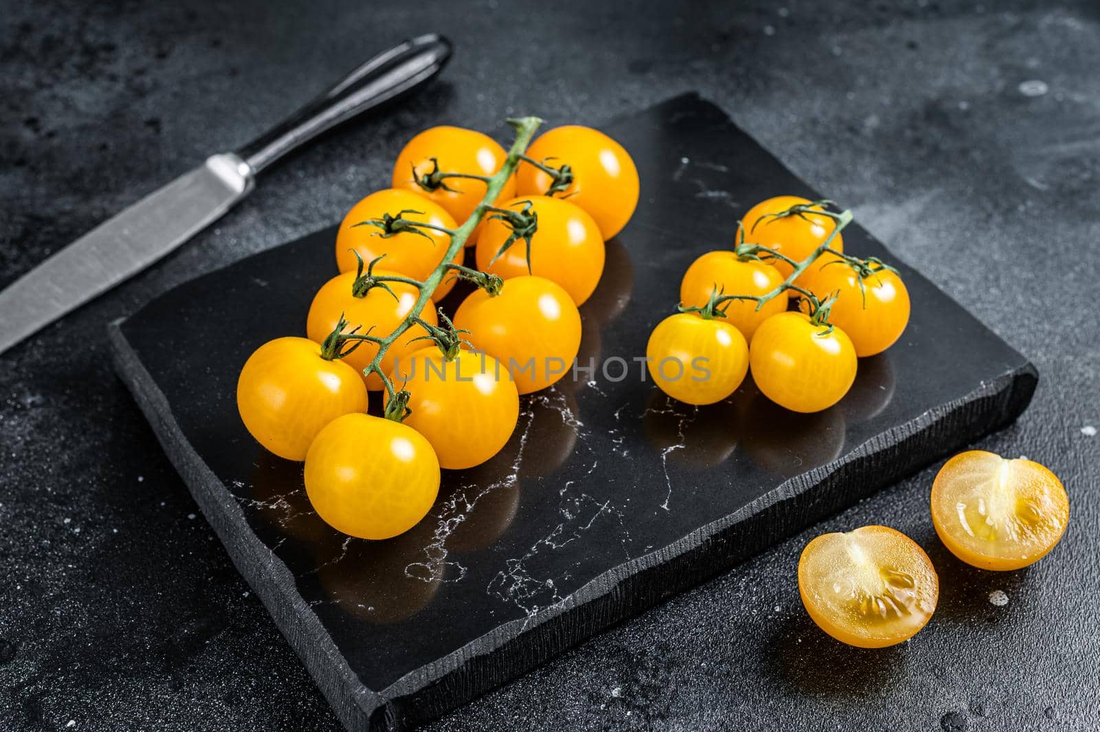 Bunch of yellow cherry tomato on a marble board. Black background. Top view by Composter