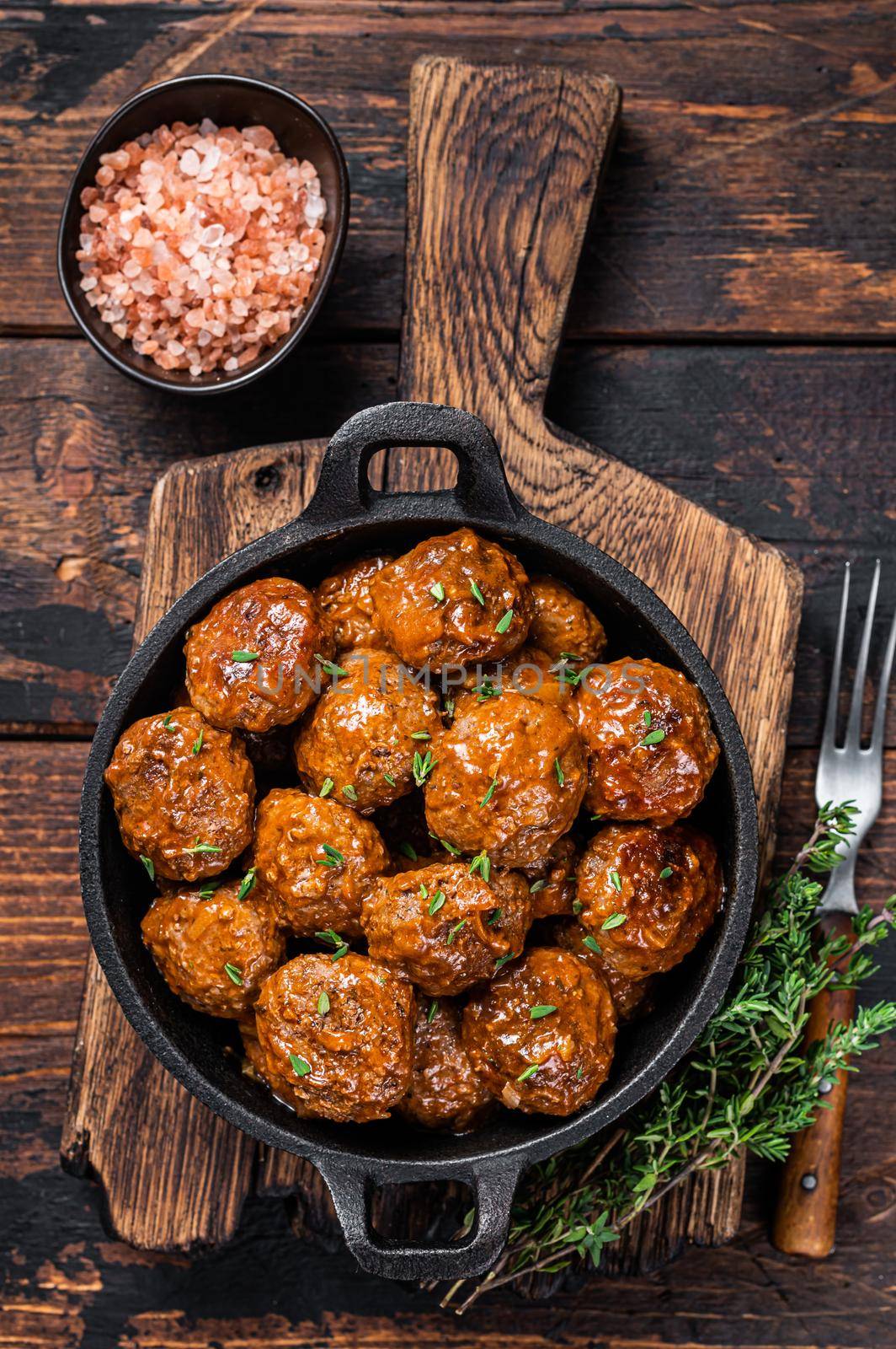 Meatballs in tomato sauce from beef and pork meat with thyme in rustic pan. Dark background. Top view.