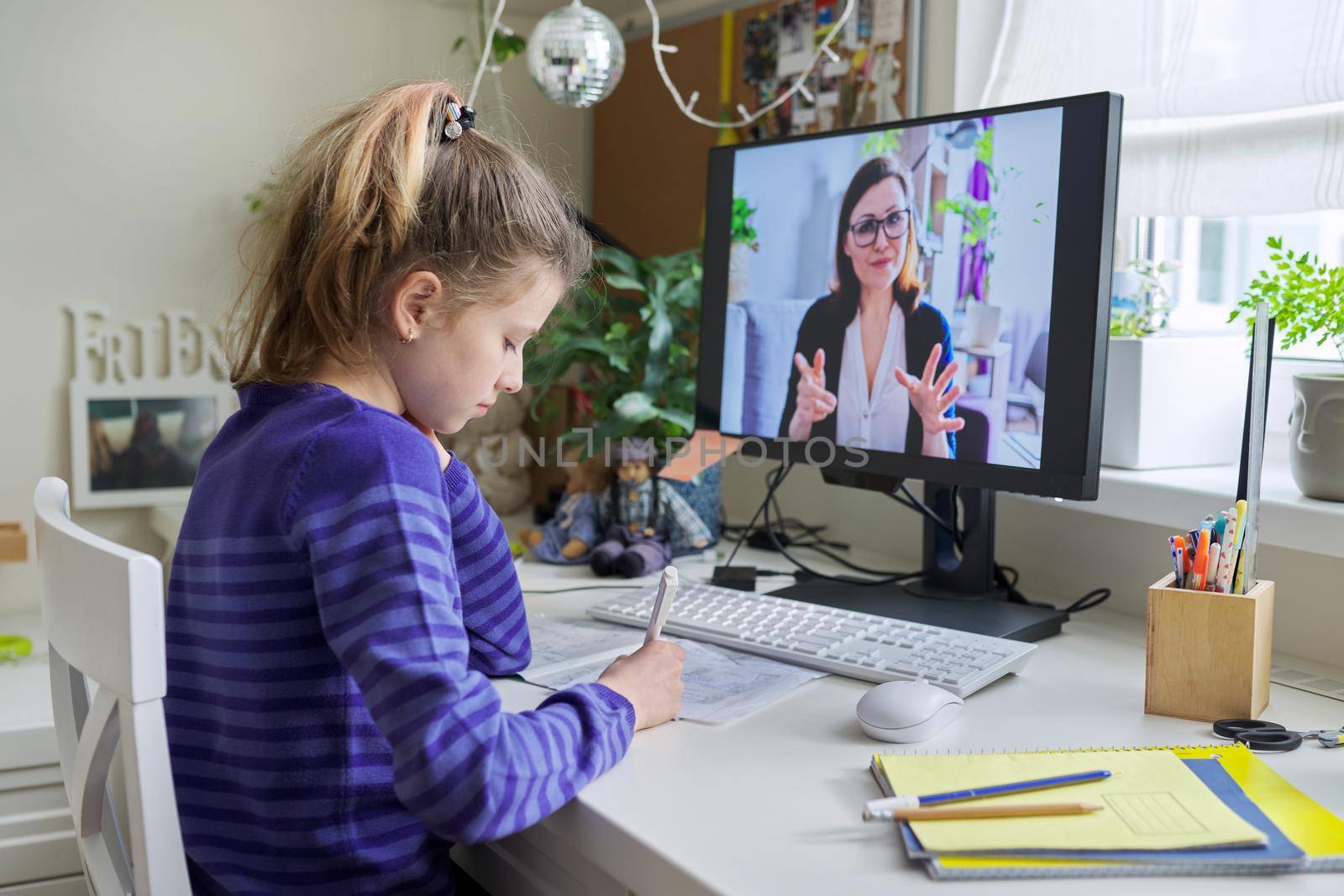 Young child girl studying with teacher remotely on computer using video call, an individual online lesson, videoconference application. Education, technology, children, pre-teens, e-learning concept