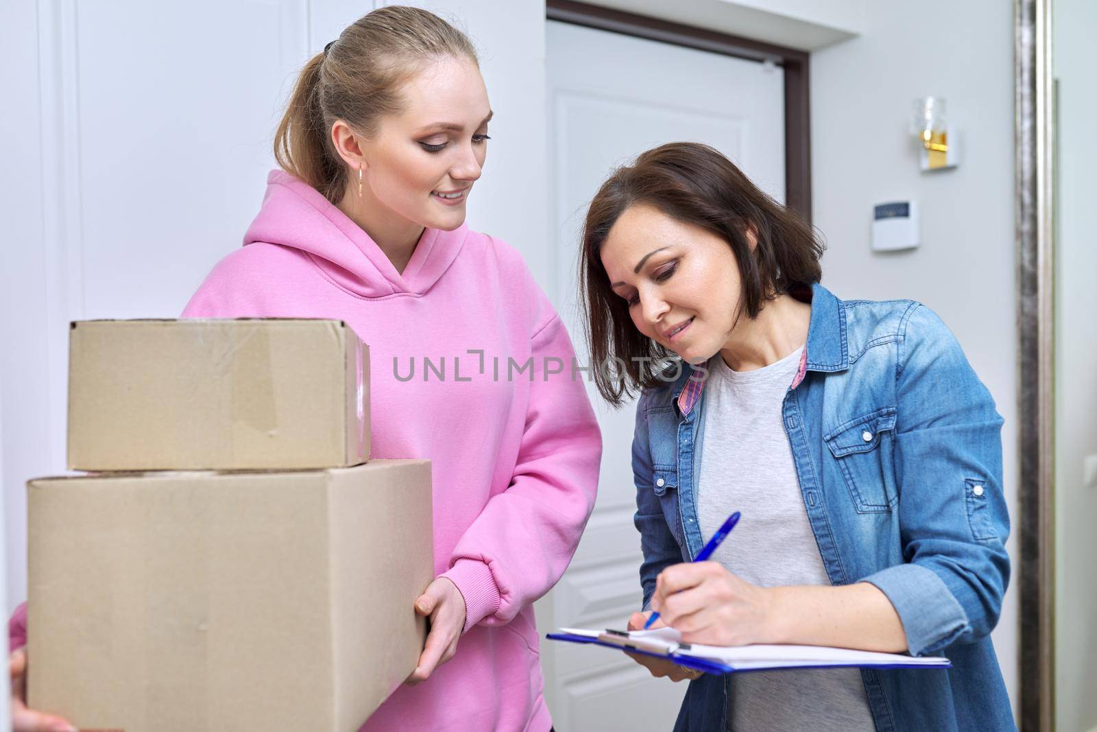 Online shopping delivery service, courier young woman with cardboard boxes near front door in apartment, adult woman buyer takes boxes