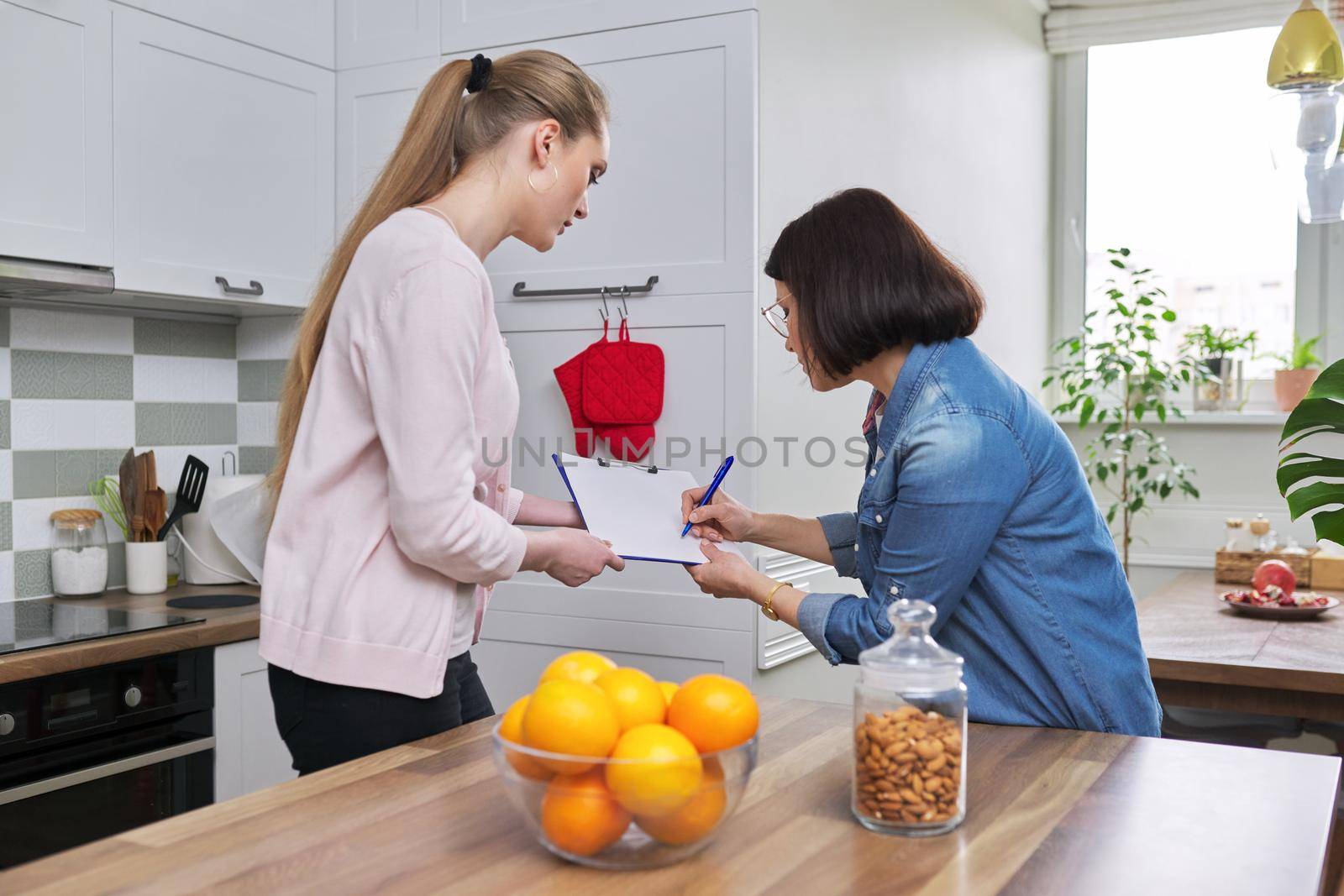 Poll, interview, monitoring, visitor young woman social worker talking and interrogating mature woman housewife, home kitchen interior background