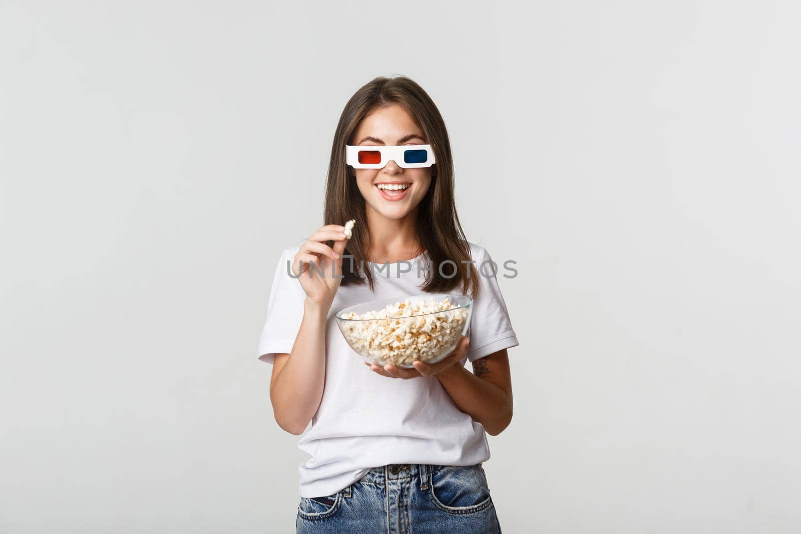 Amused pretty young woman in 3d glasses watching movies or tv series, eating popcorn and smiling thrilled by Benzoix