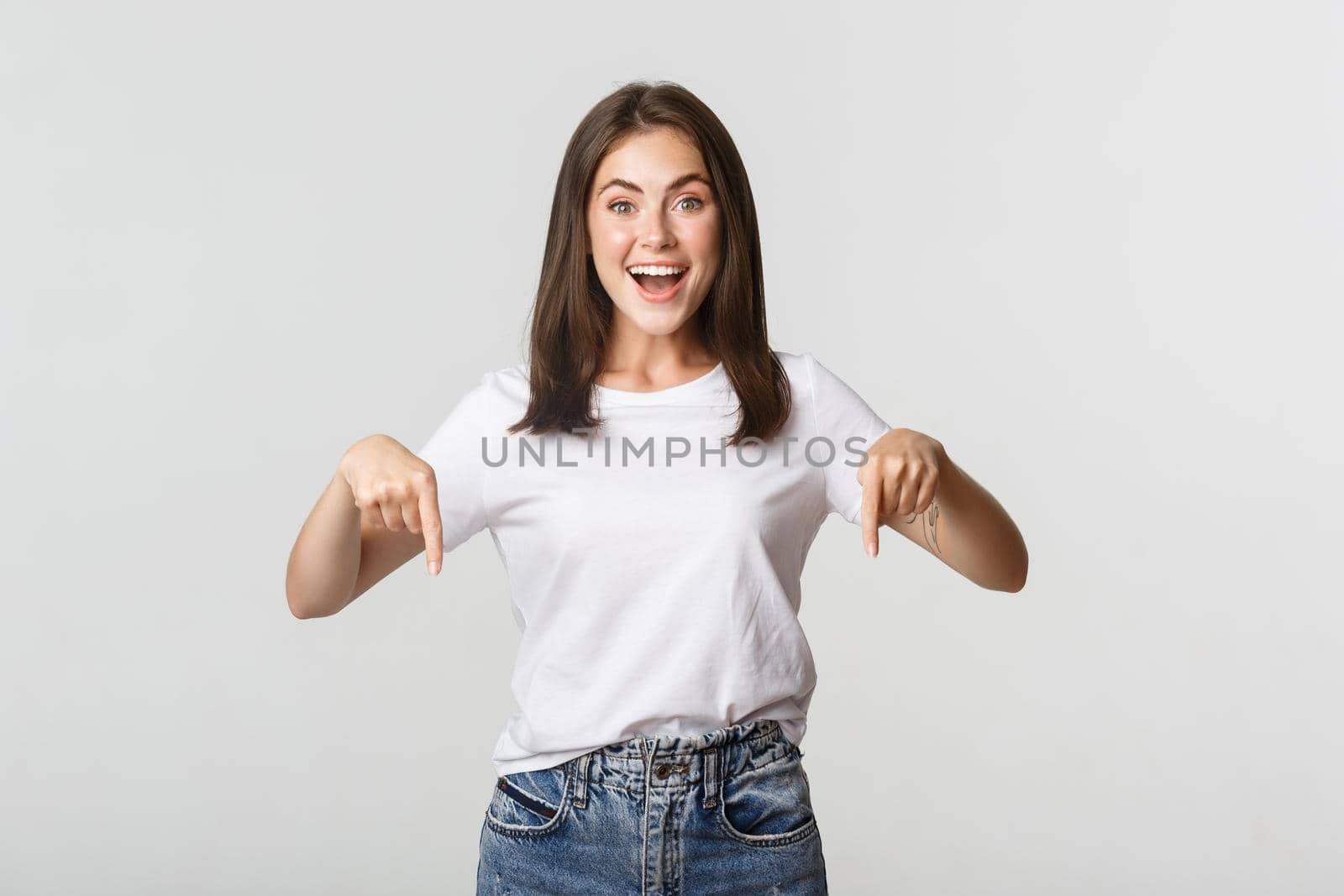 Satisfied smiling brunette girl pointing fingers down, recommend product by Benzoix